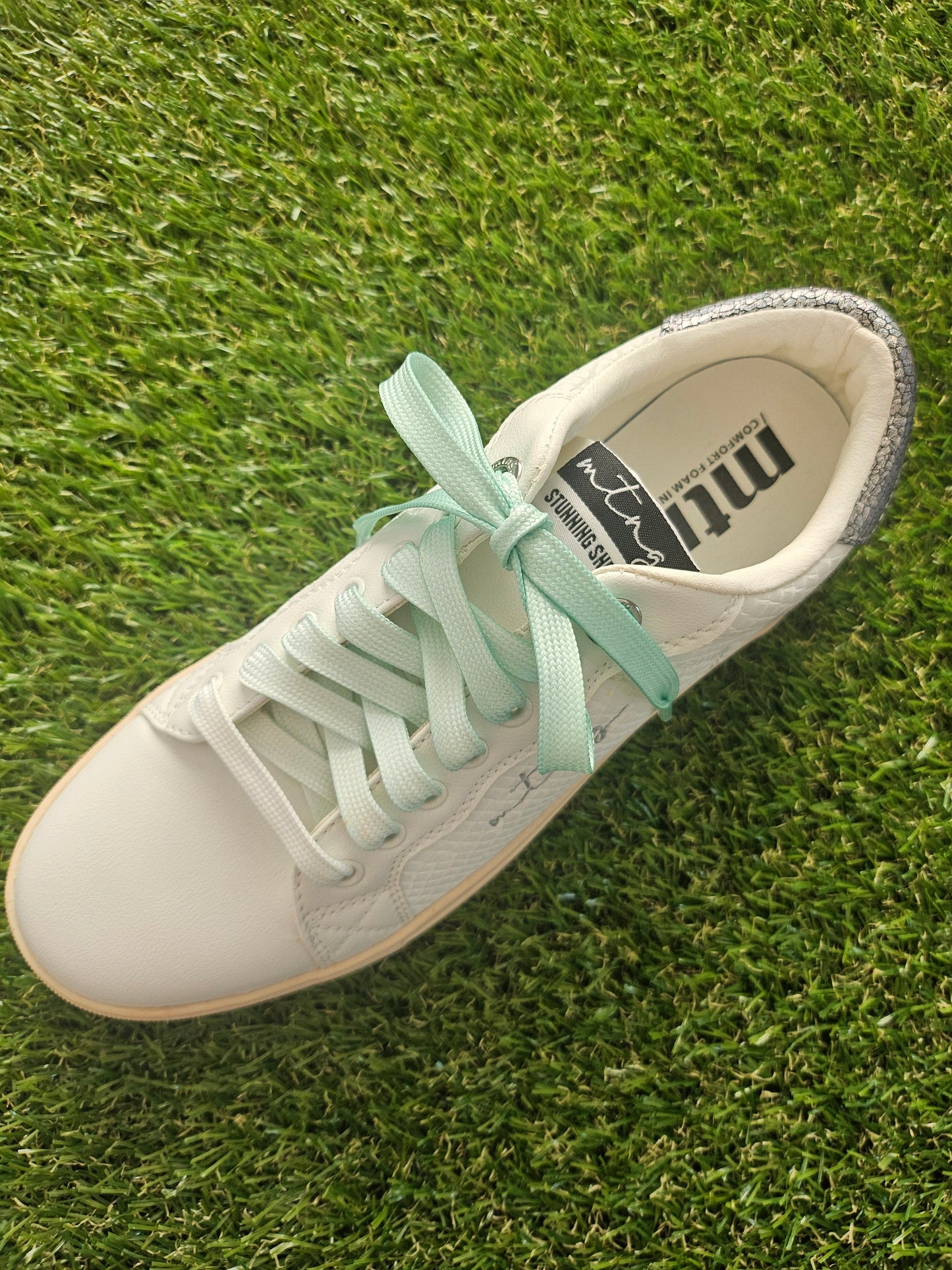White sneaker with light green laces on grass