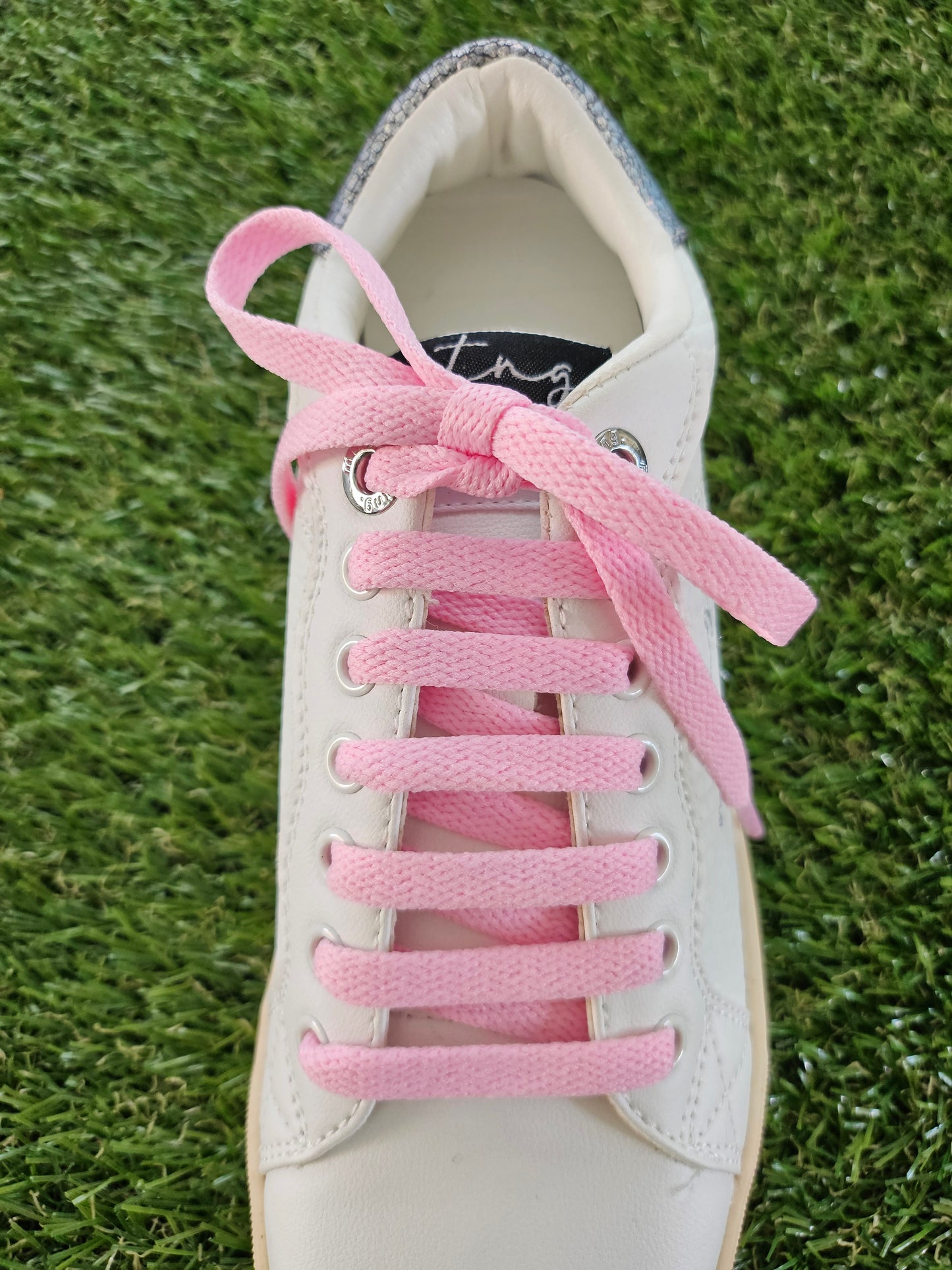 White sneaker with pink laces on a grass background
