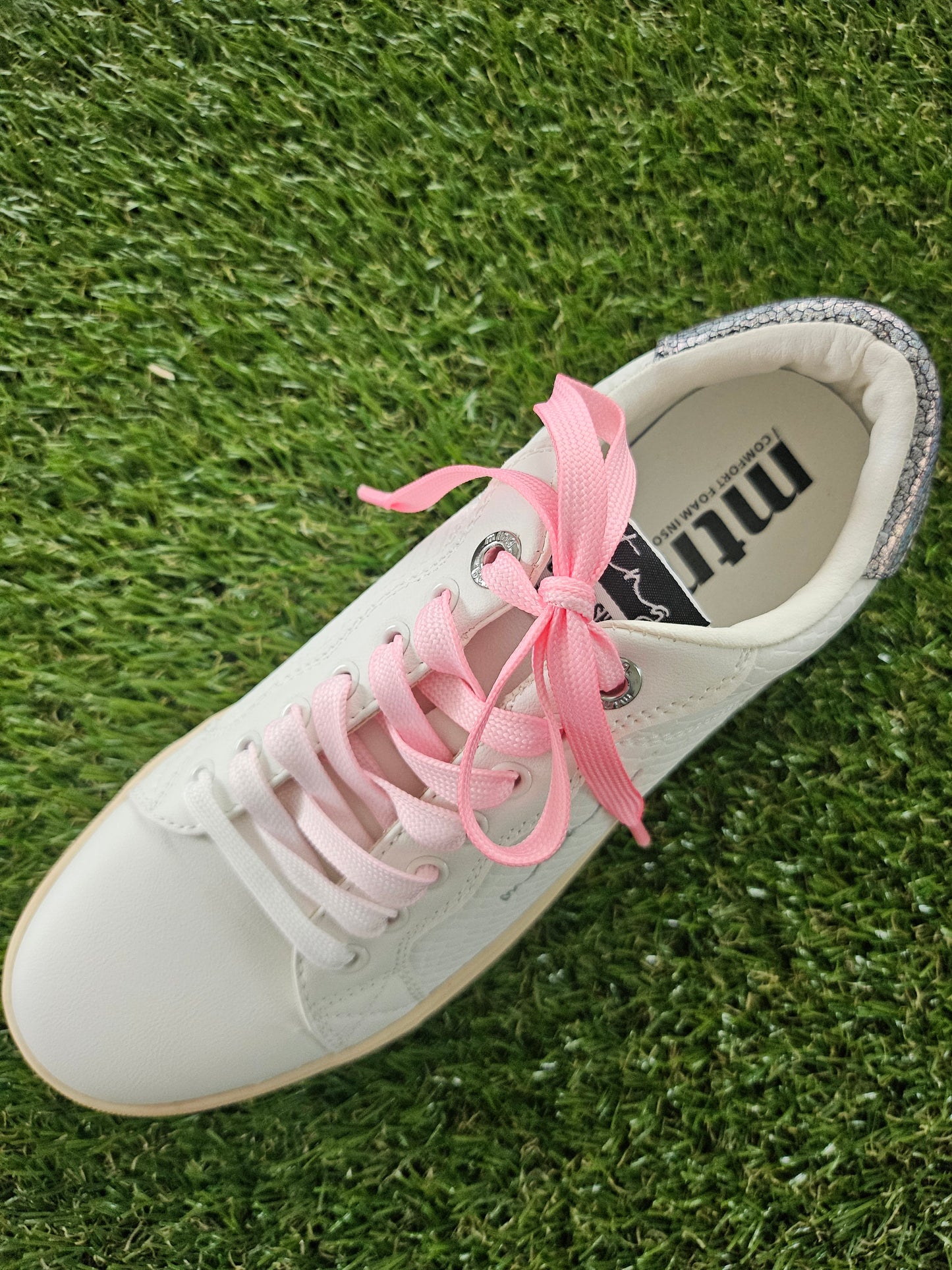 White sneaker with pink tie dye laces on grass
