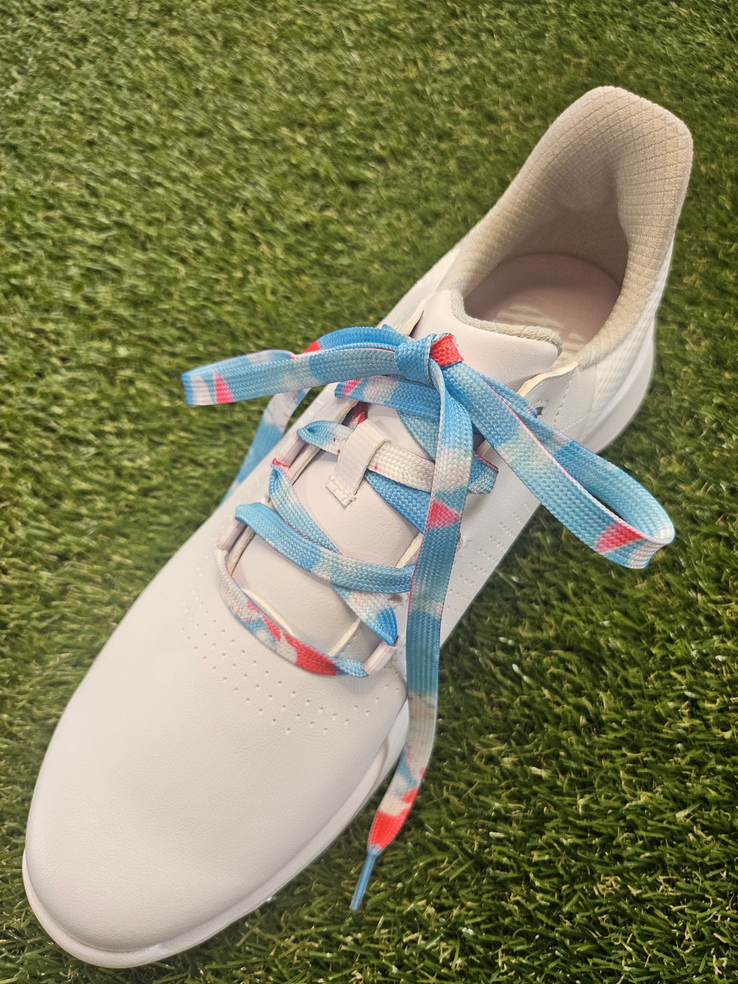 White ladies golf shoe with colorful laces on a grass background
