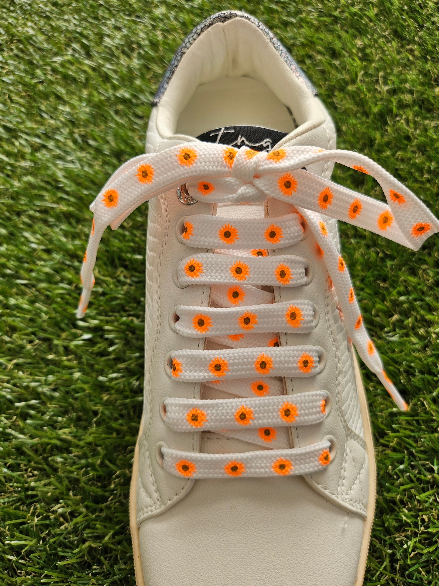 Sneaker with white laces featuring orange floral patterns on a grass background