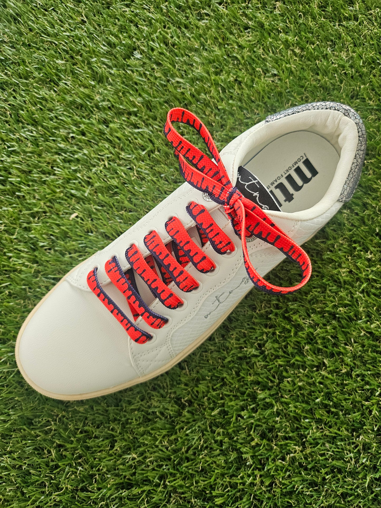 Red paint drip shoelaces in white trainers on grass