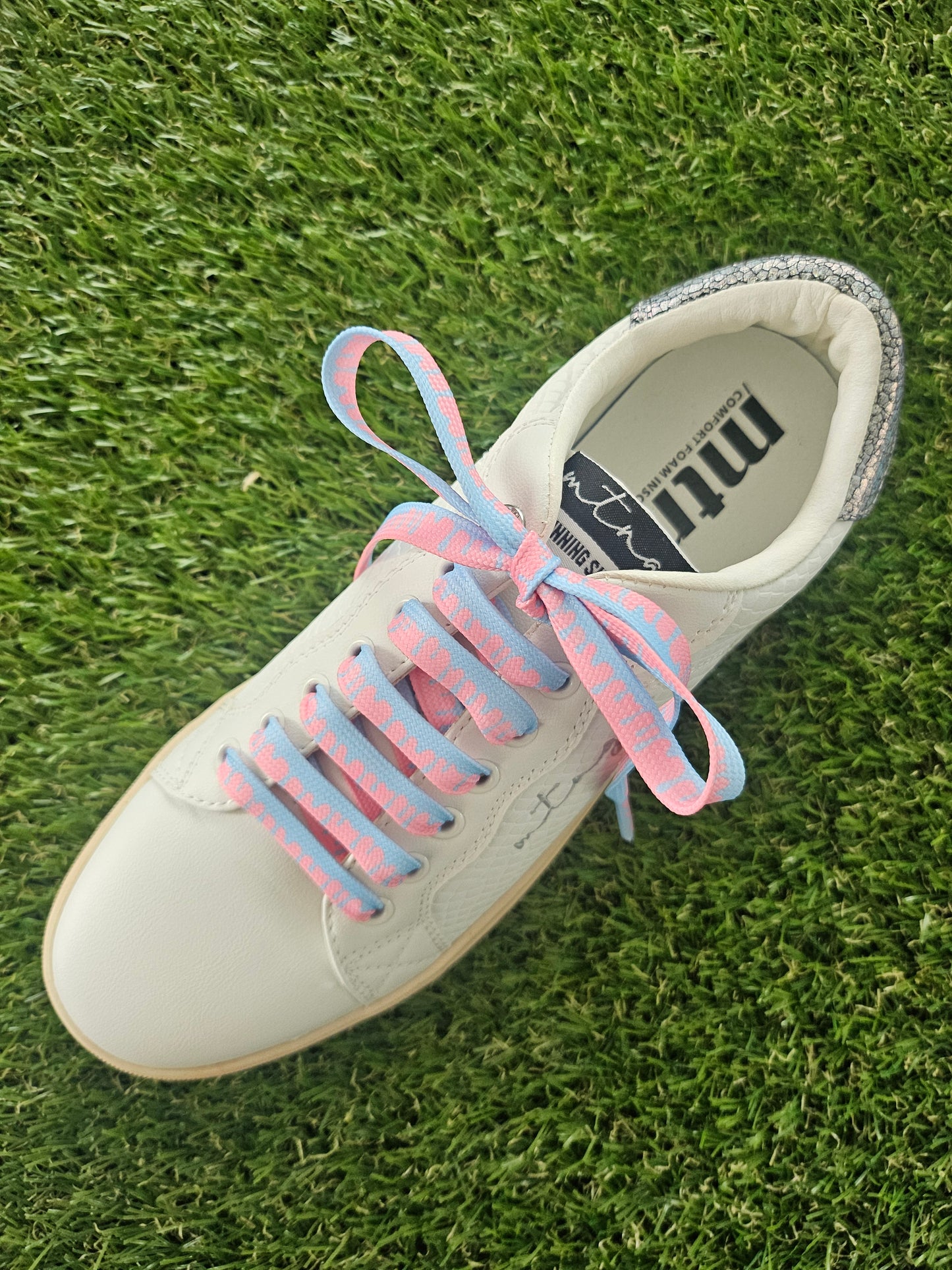 White sneaker with pink and blue shoelaces on grass