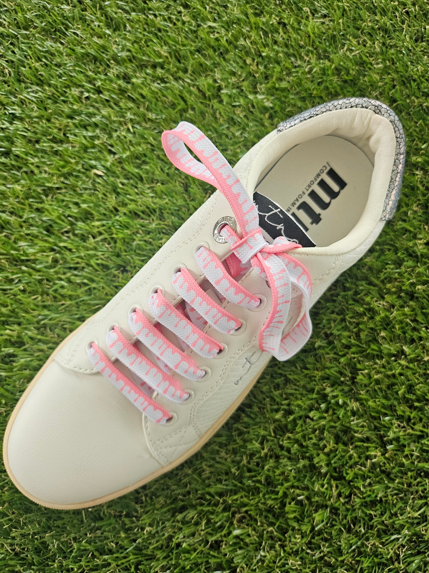 White sneaker with pink laces on grass
