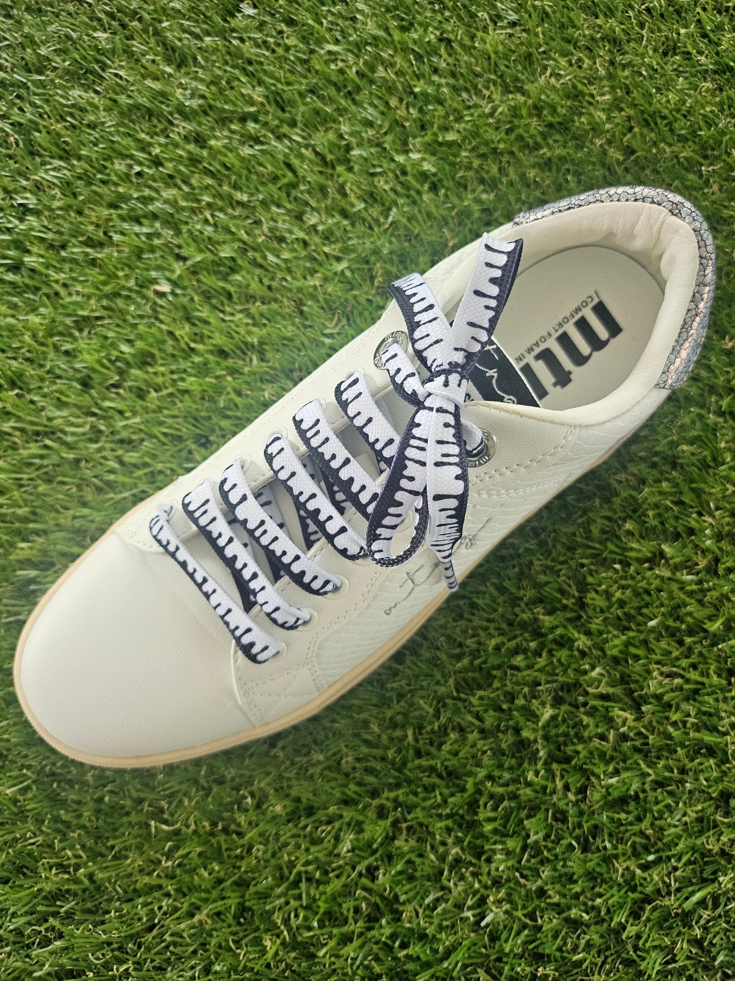 White sneaker with black and white paint drip design shoelaces on a grass background