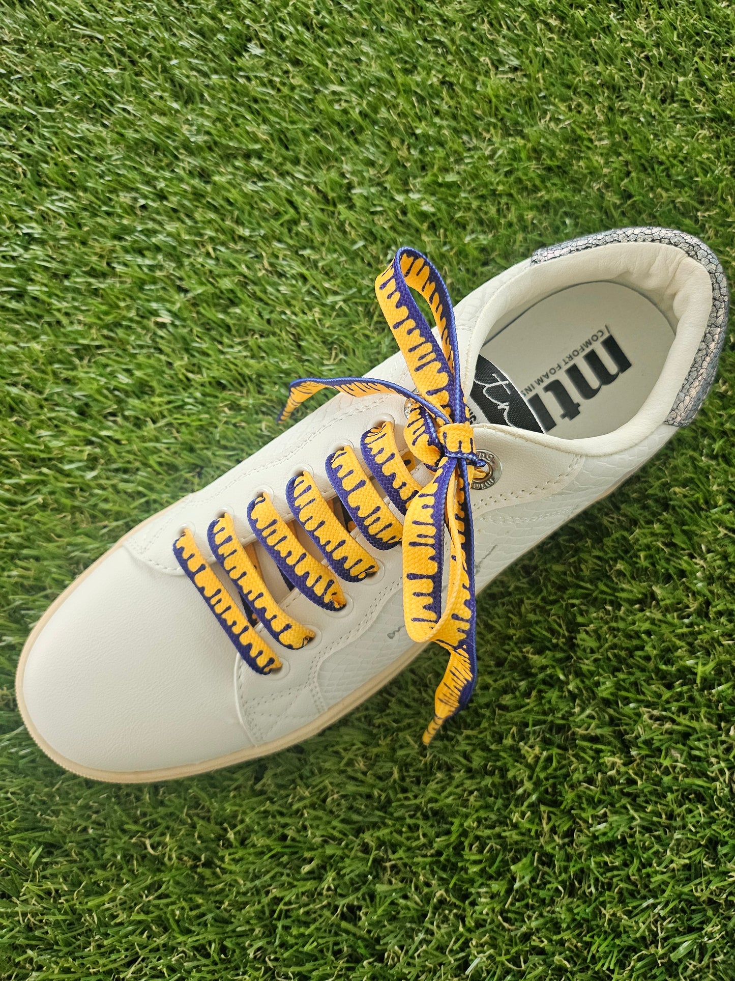 White shoe with yellow and blue laces on grass