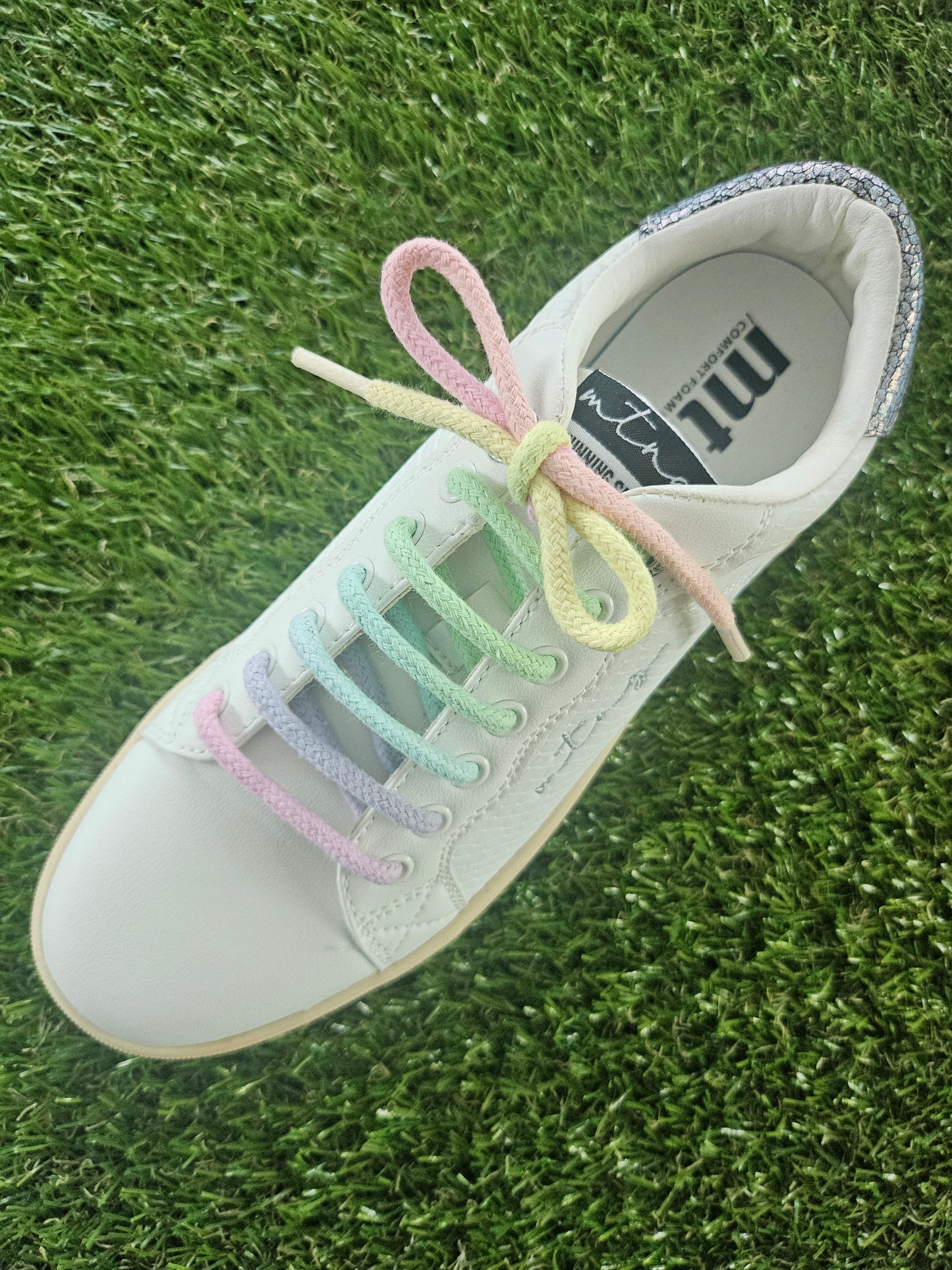 White sneaker with pastel shoelaces on a grass background