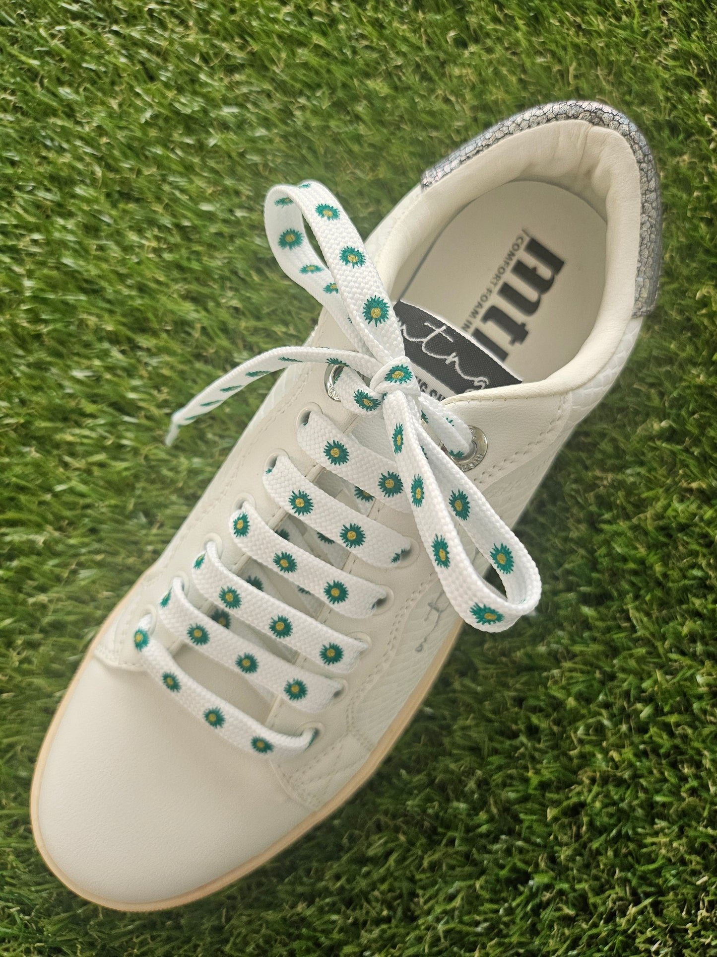 White sneaker with green flowers on white shoe laces on grass