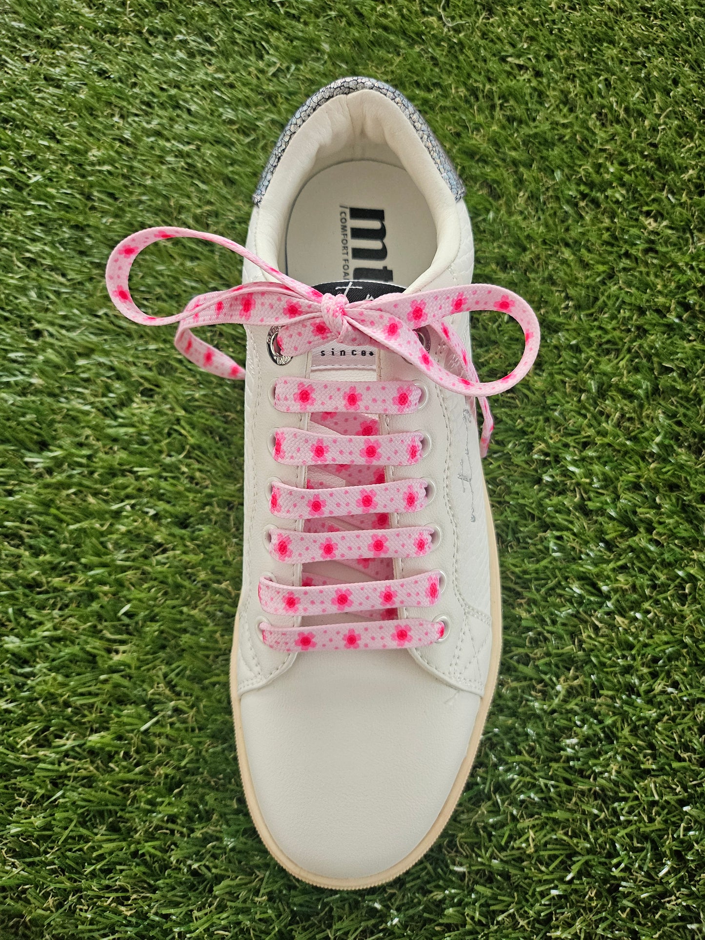 White sneaker with pink shoelaces on a grass background