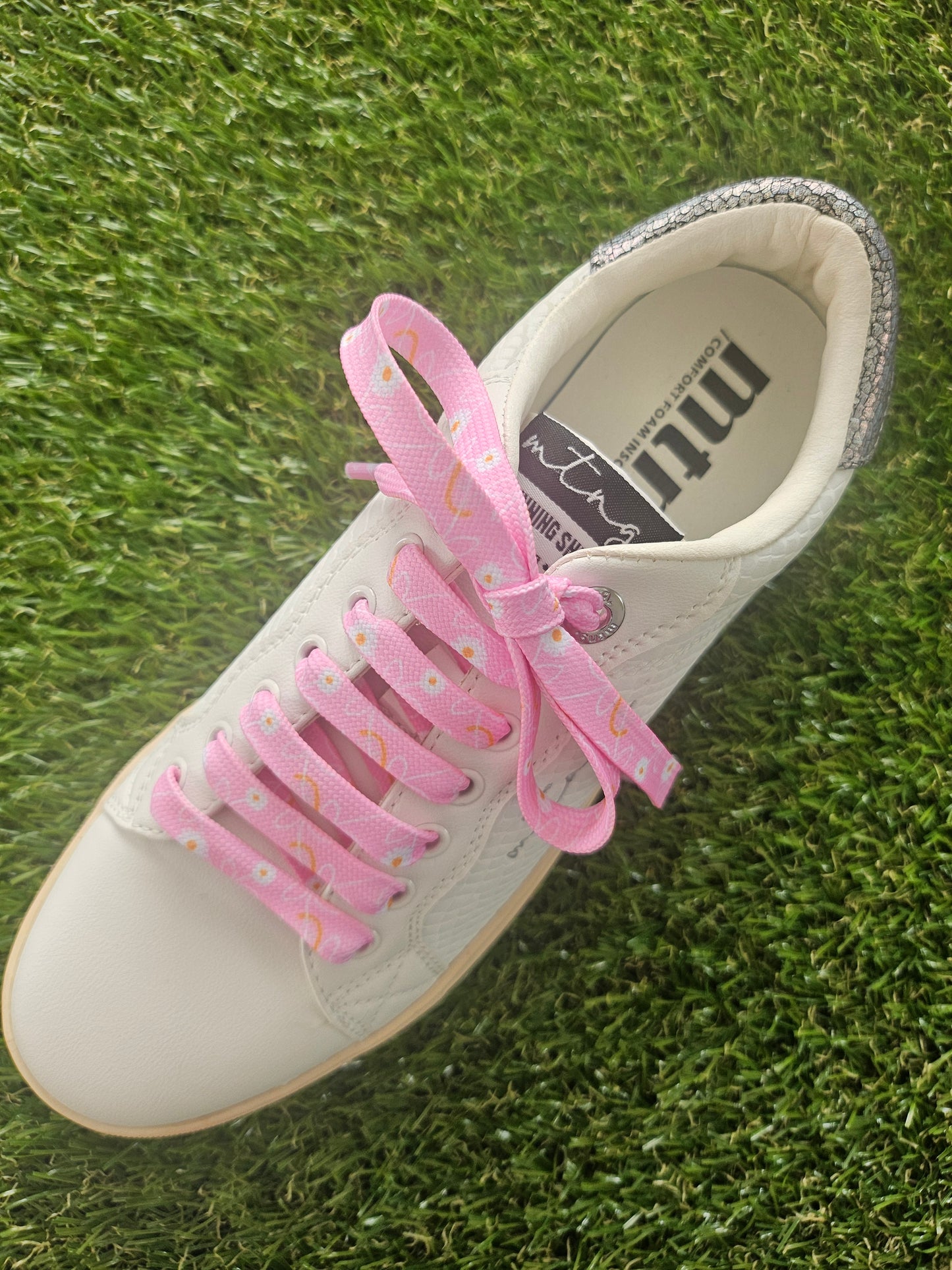 White sneaker with pink floral laces on grass