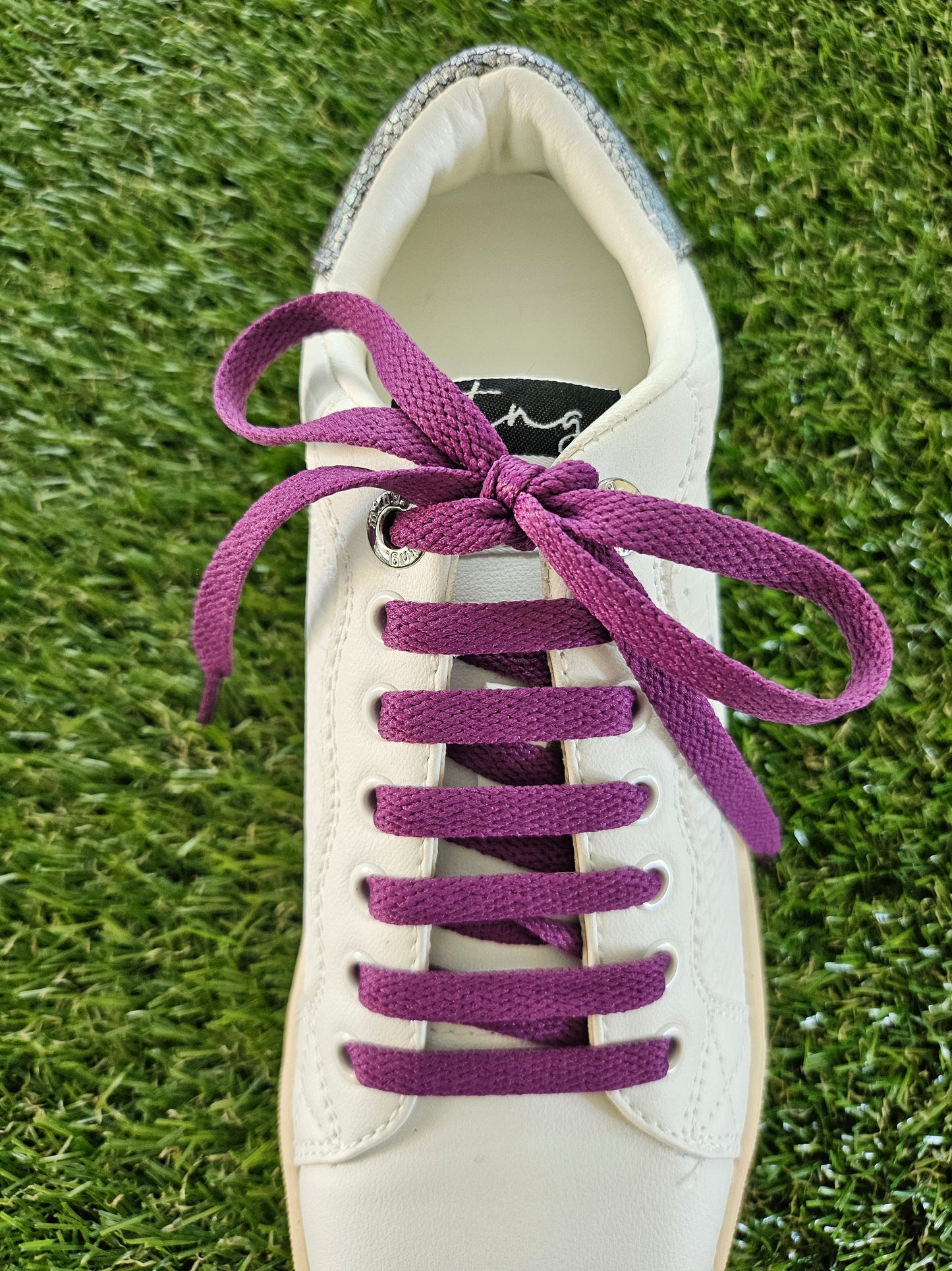 White sneaker with purple laces on a grass background
