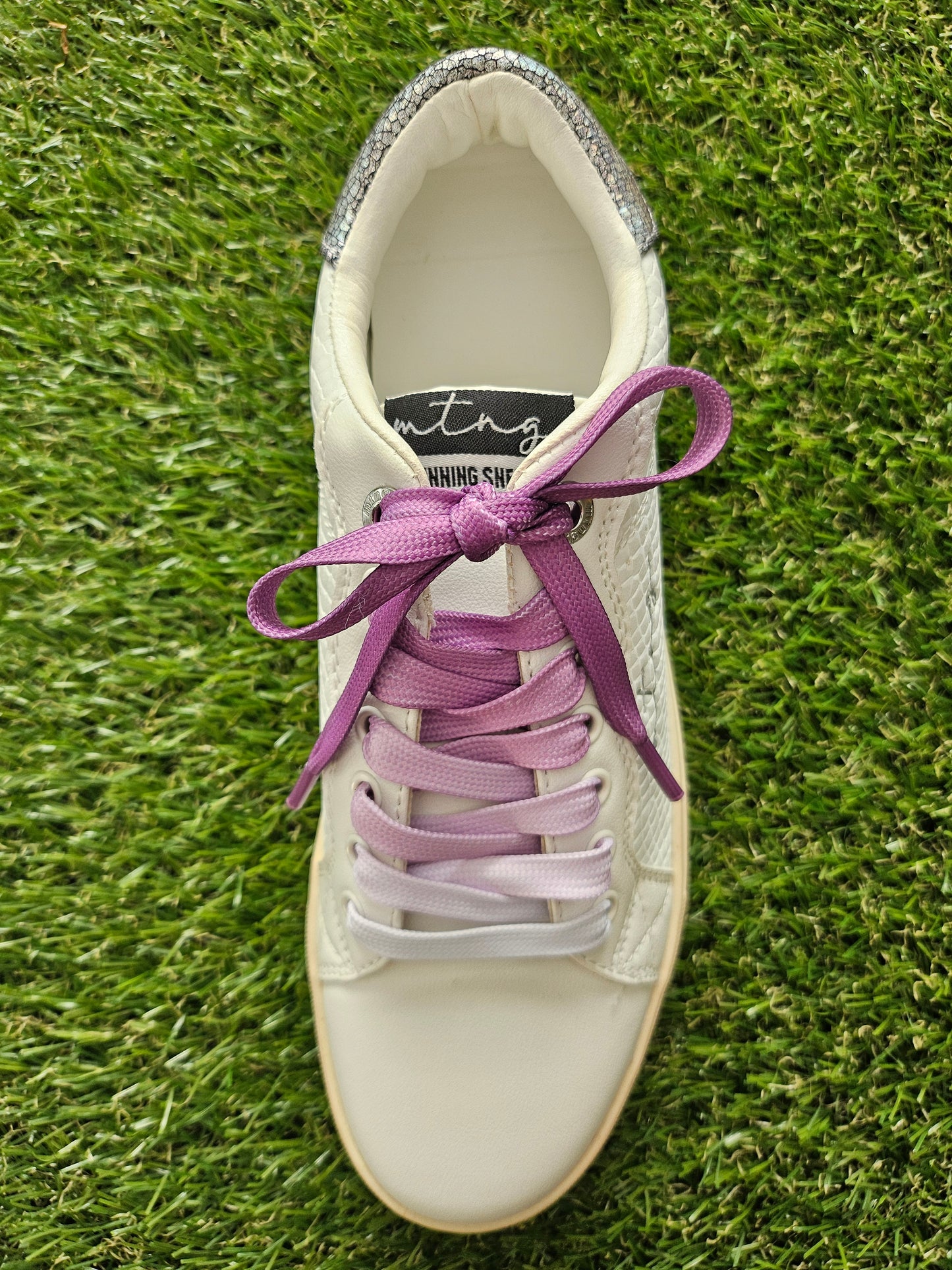 White sneaker with purple laces on a grass background