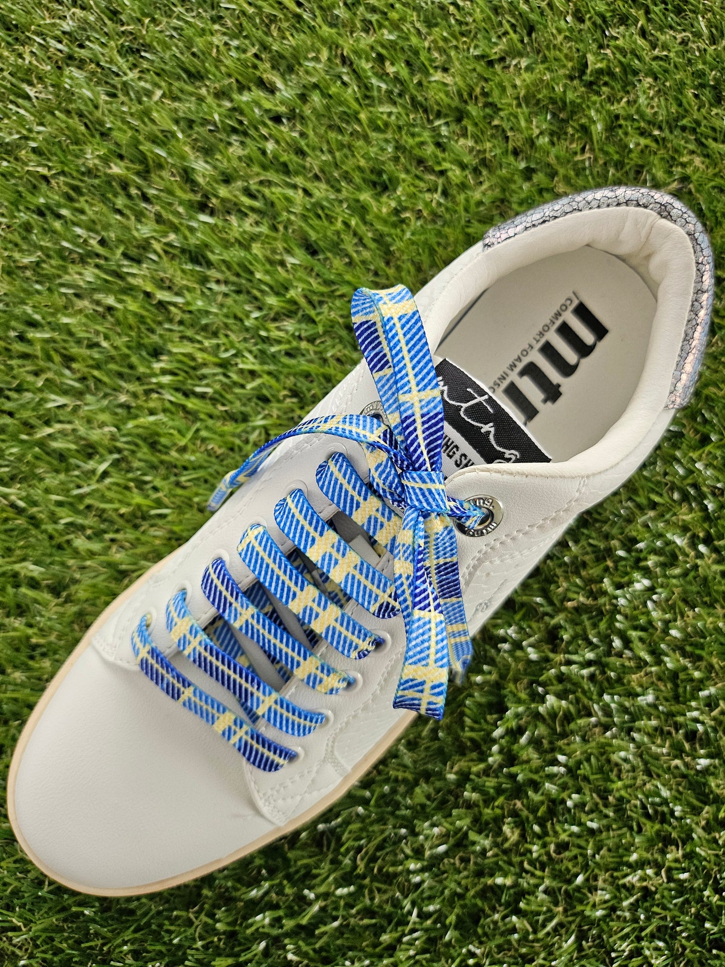 White shoe with blue and yellow plaid laces on grass