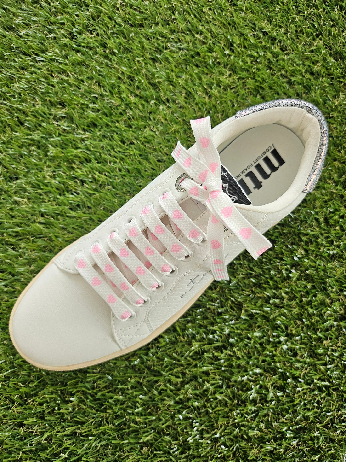White sneaker with pink heart laces on grass