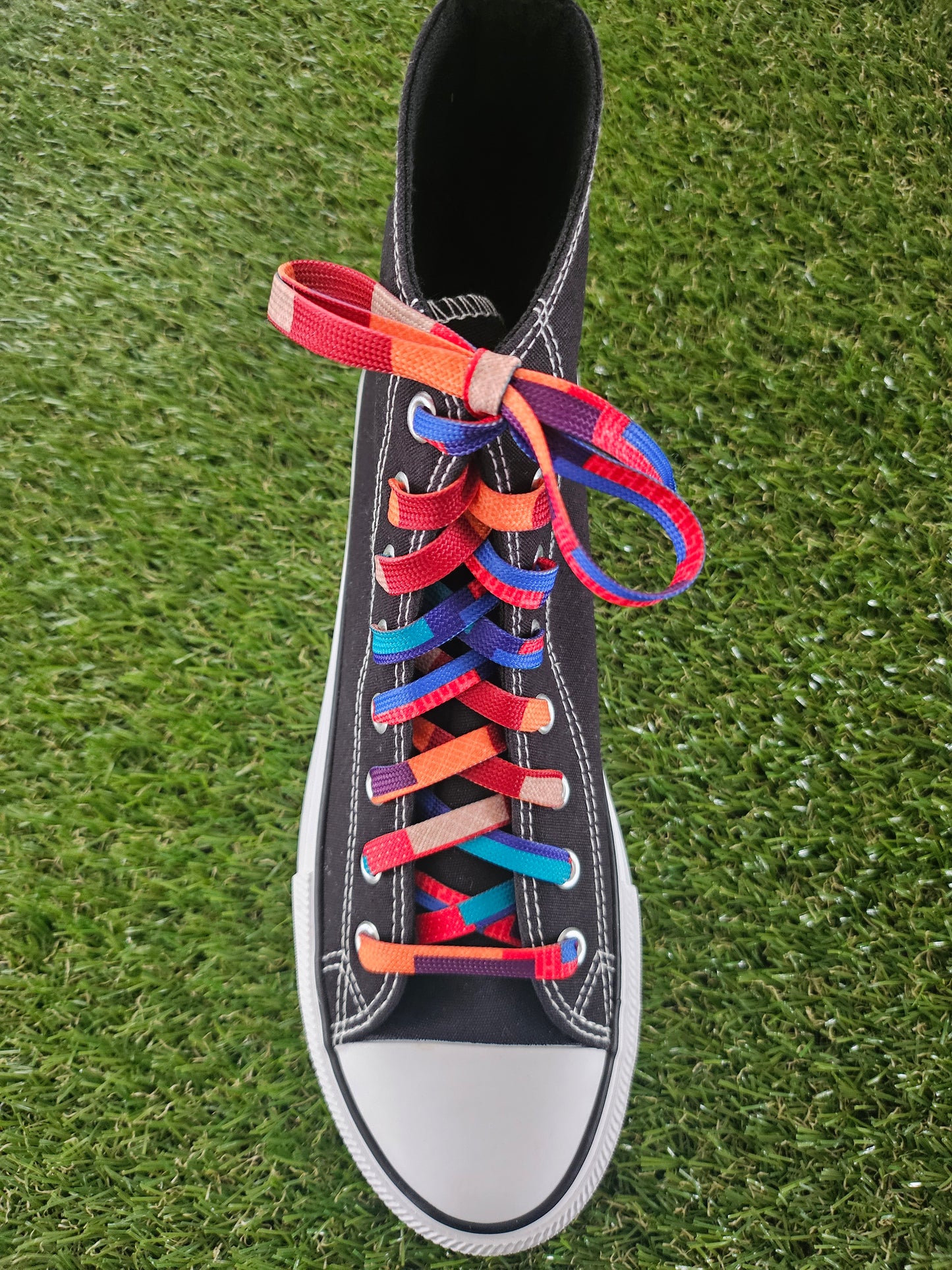 Black high-top sneaker with colourful laces on a grass background