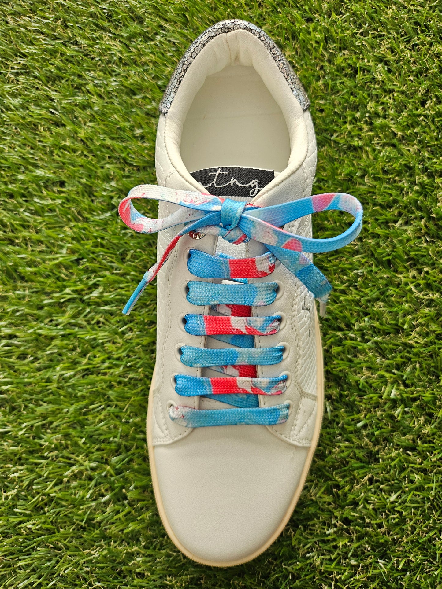 White sneaker with colorful laces on a grass background