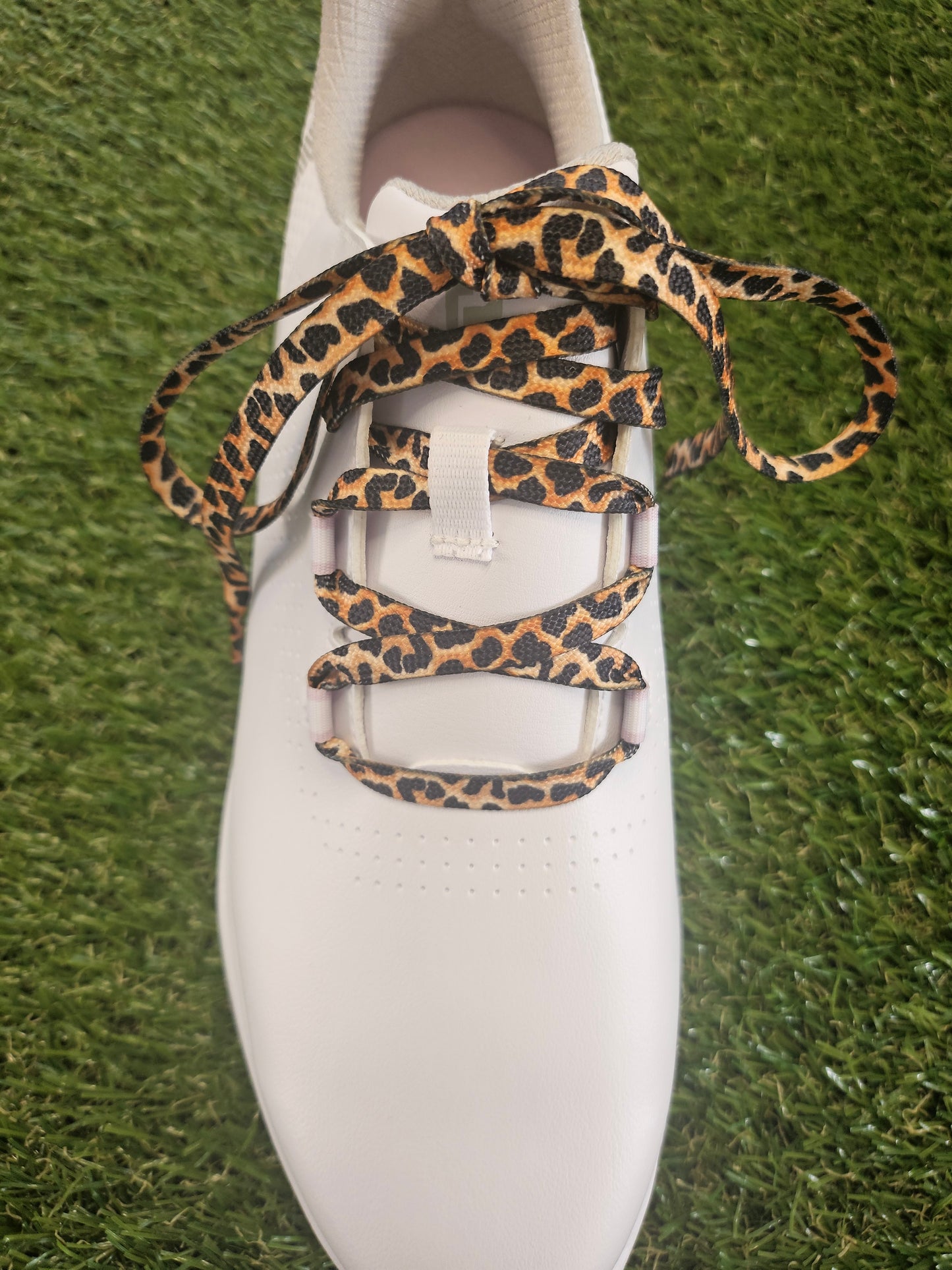 White ladies golf shoe with leopard print laces on a grass background