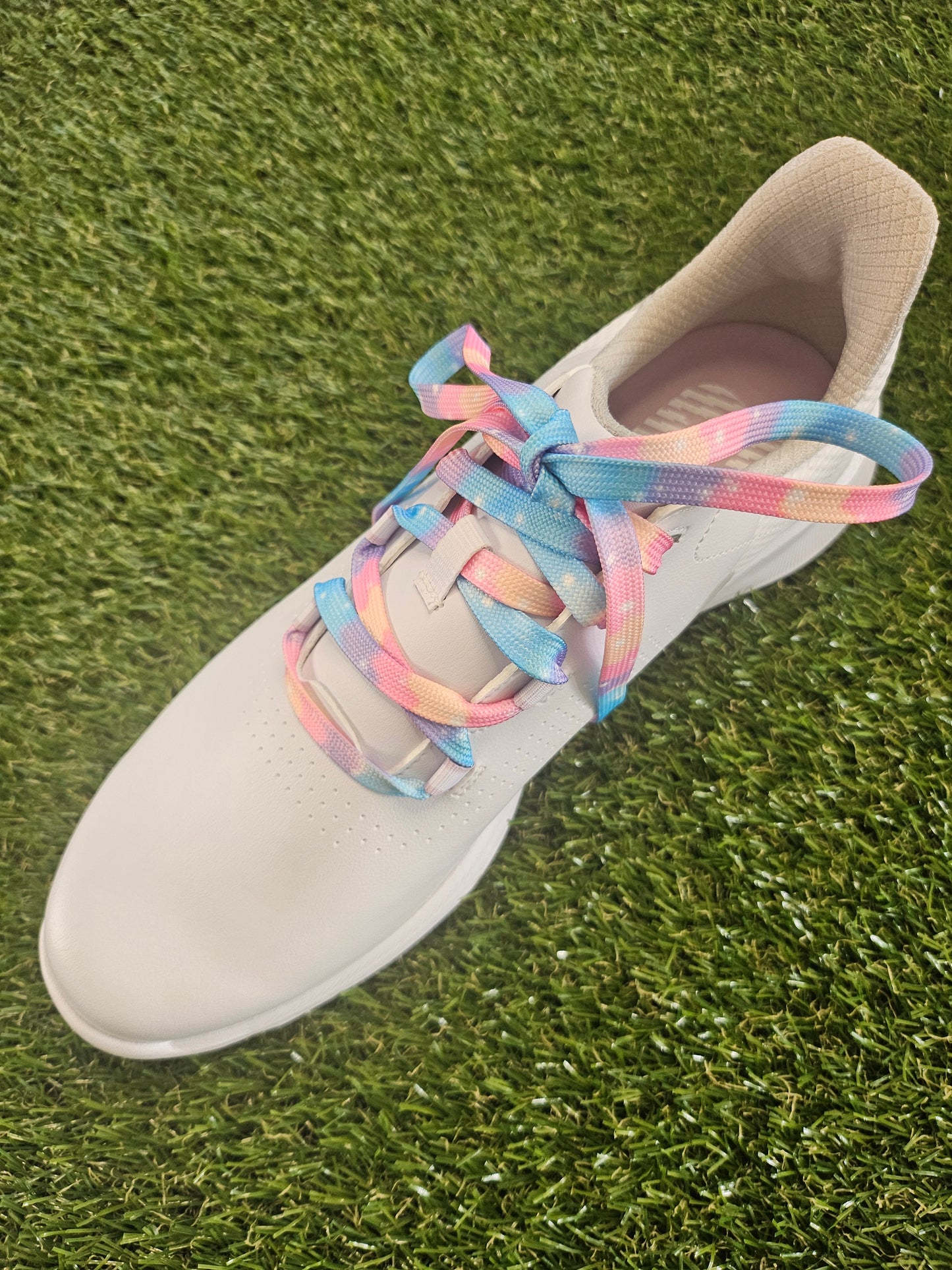 White woman's golf shoe with colourful cloudy soft pastel coloured shoelaces on a grass background