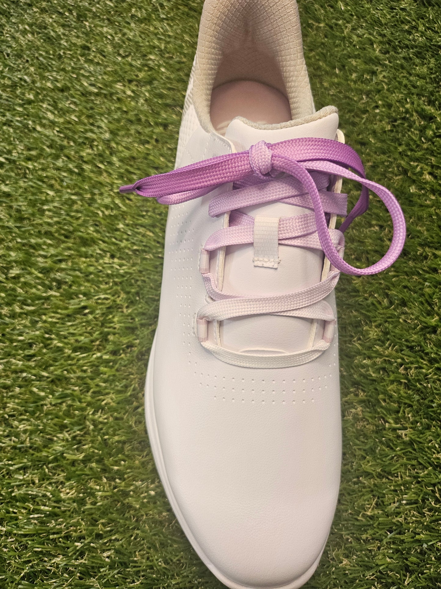 White golf shoe with purple laces accessories on a grass background