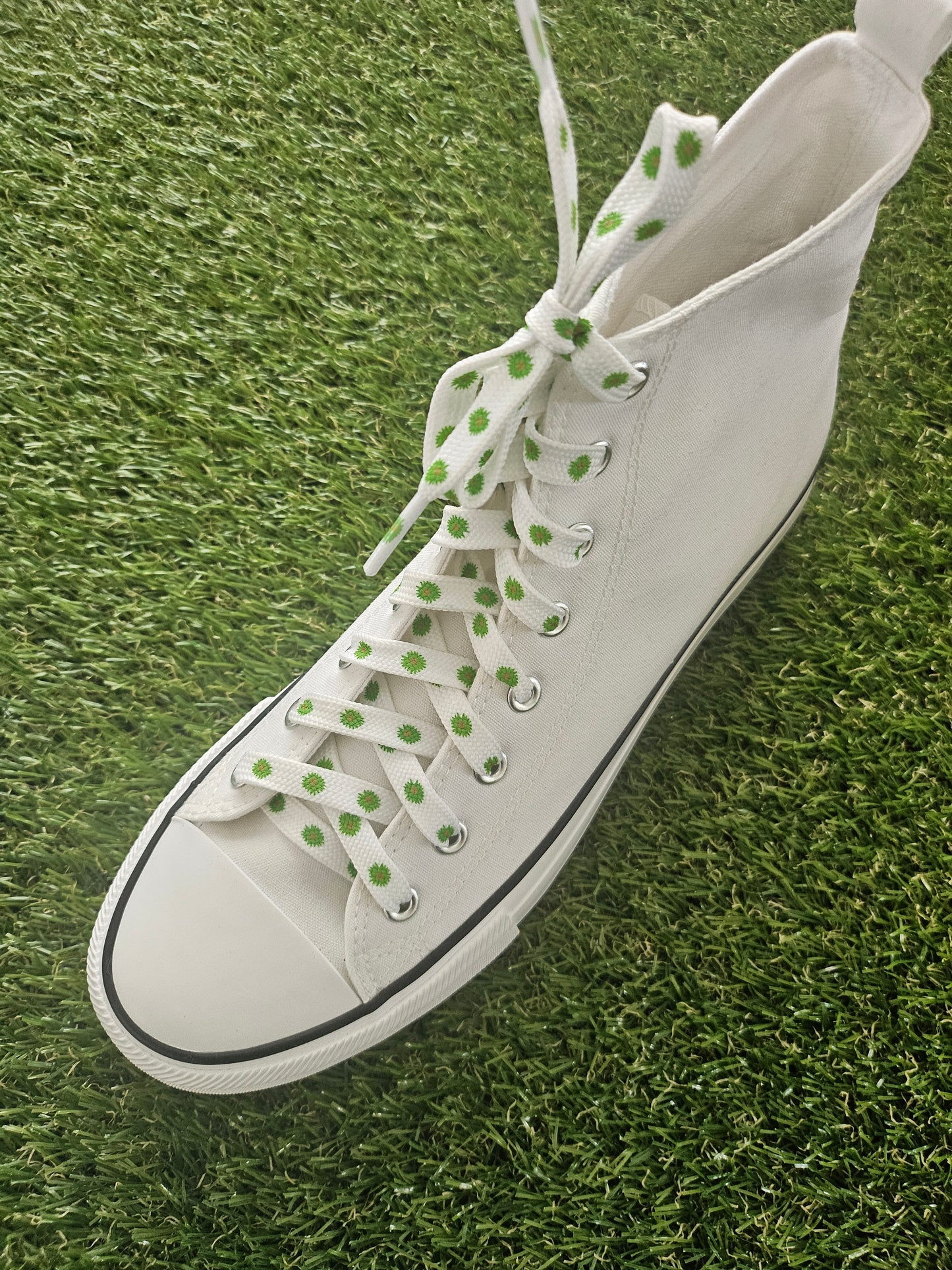 White high-top sneaker with green flowers on white laces on grass