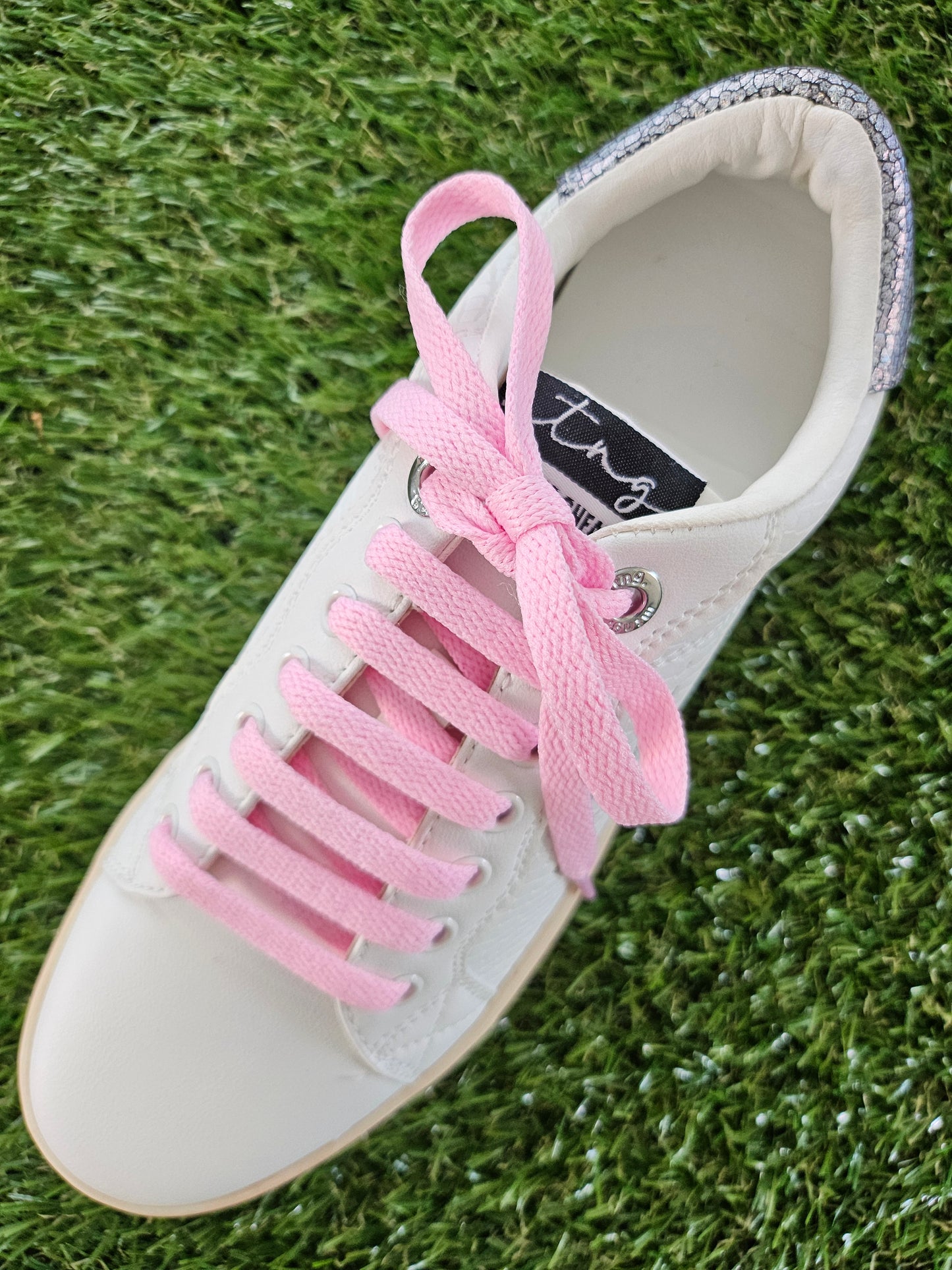 White sneaker with pink laces on a grass background