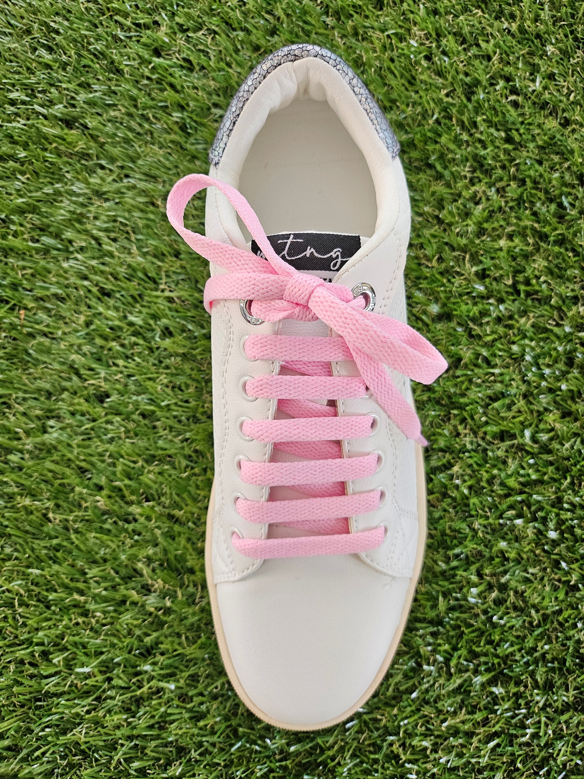 White sneaker with pink laces on a grass background