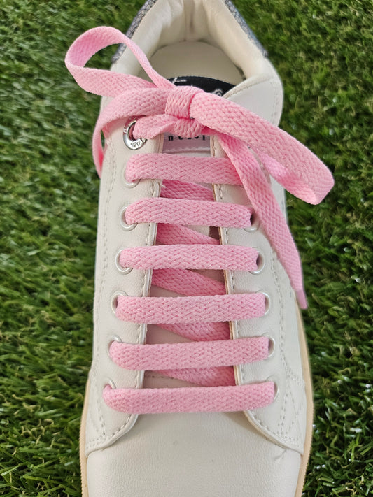 White sneaker with pink shoelaces on a grass background
