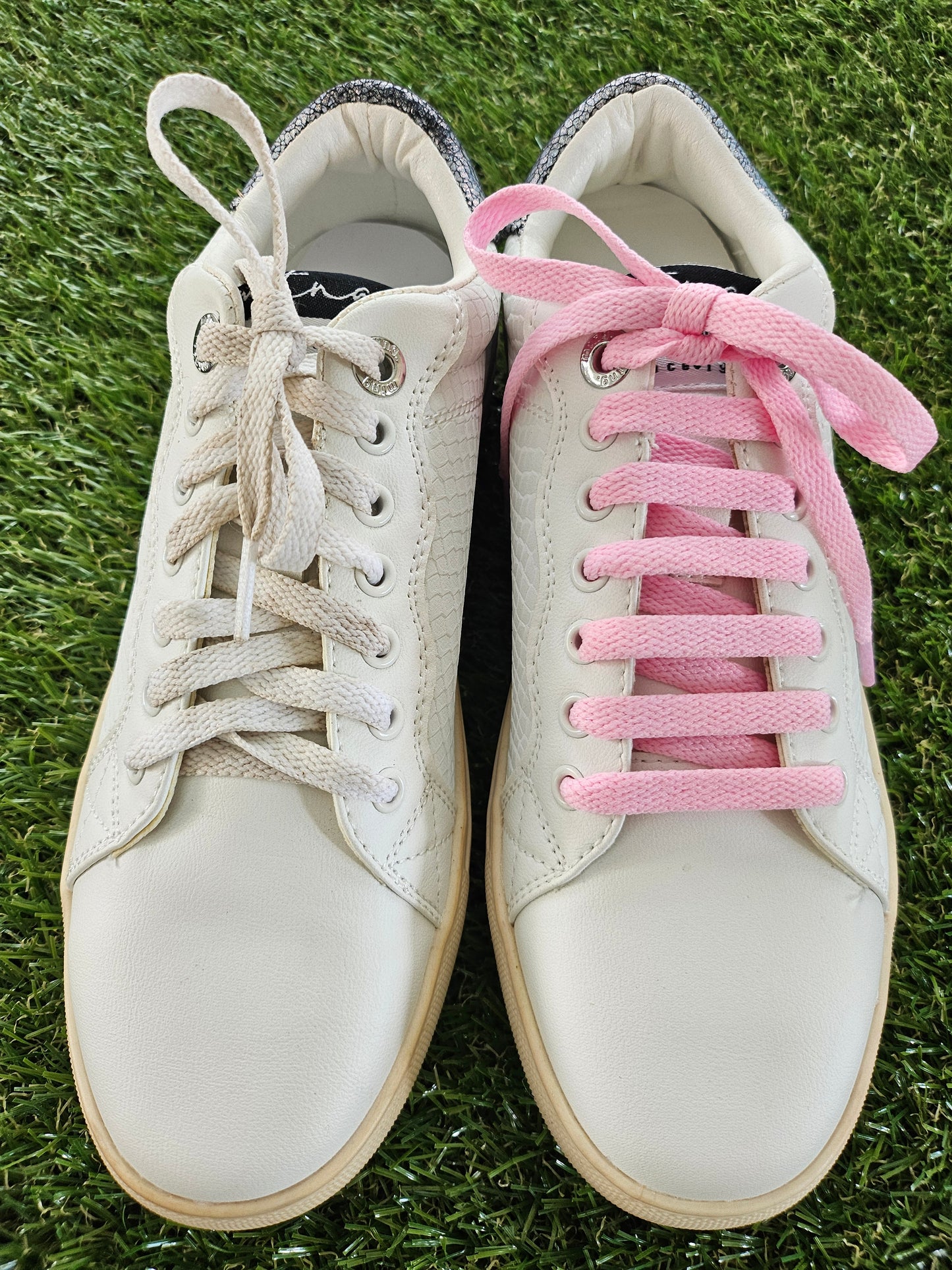 White sneakers with pink and beige laces on grass