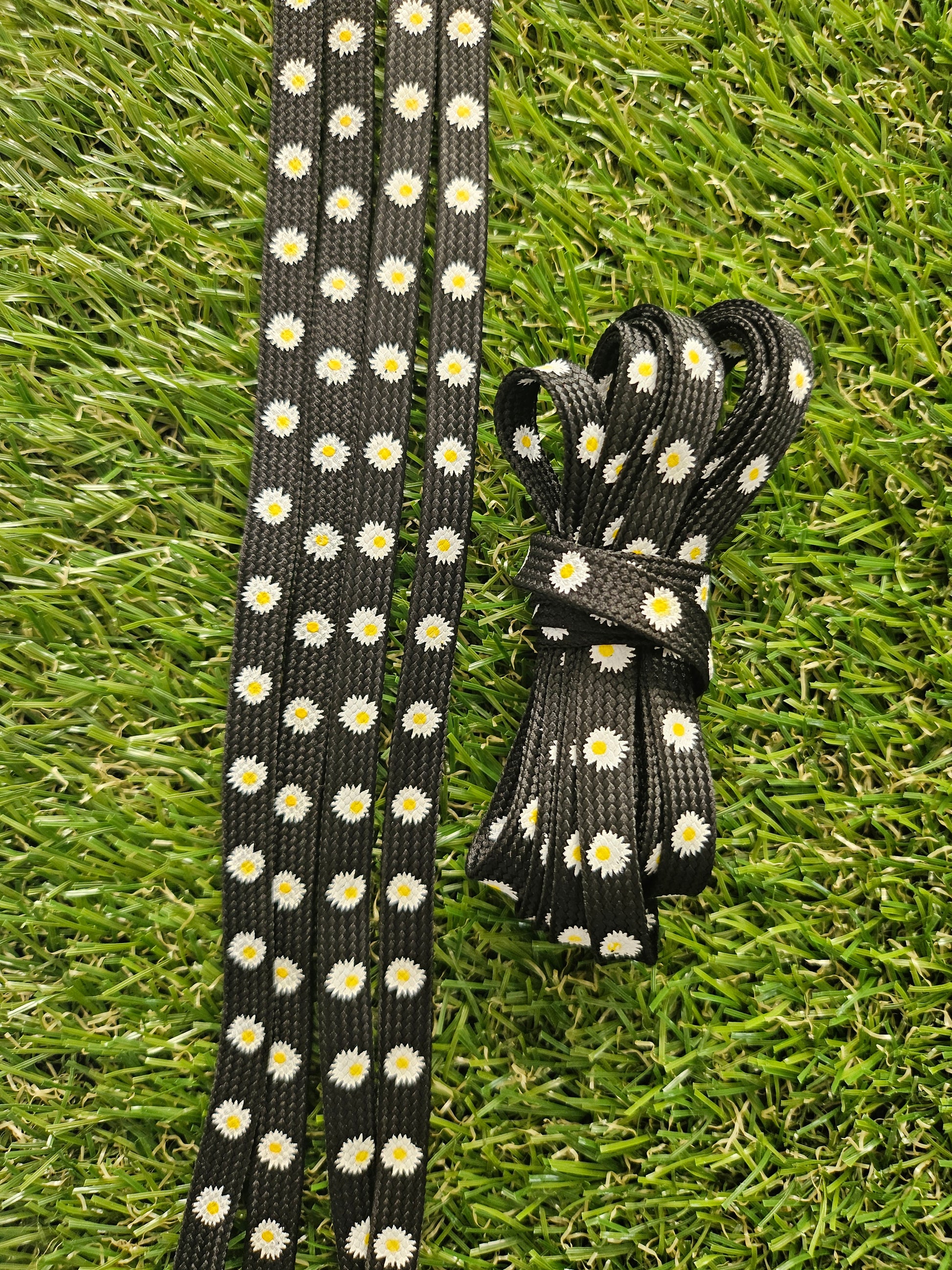 Black shoelaces with white daisy pattern on grass
