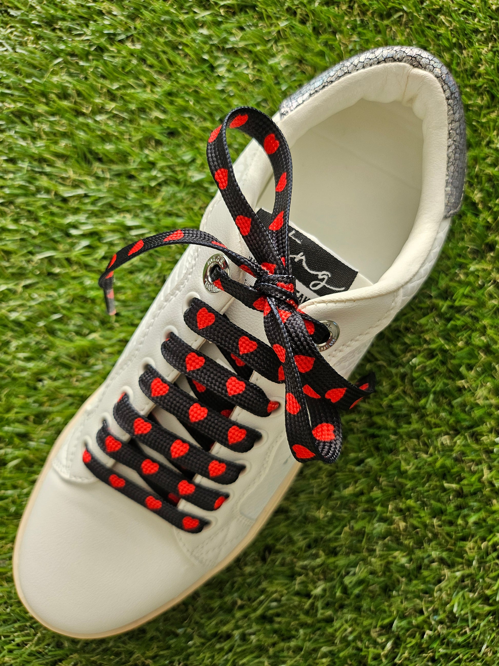 White trainers with Black shoe laces with red heart pattern on grass