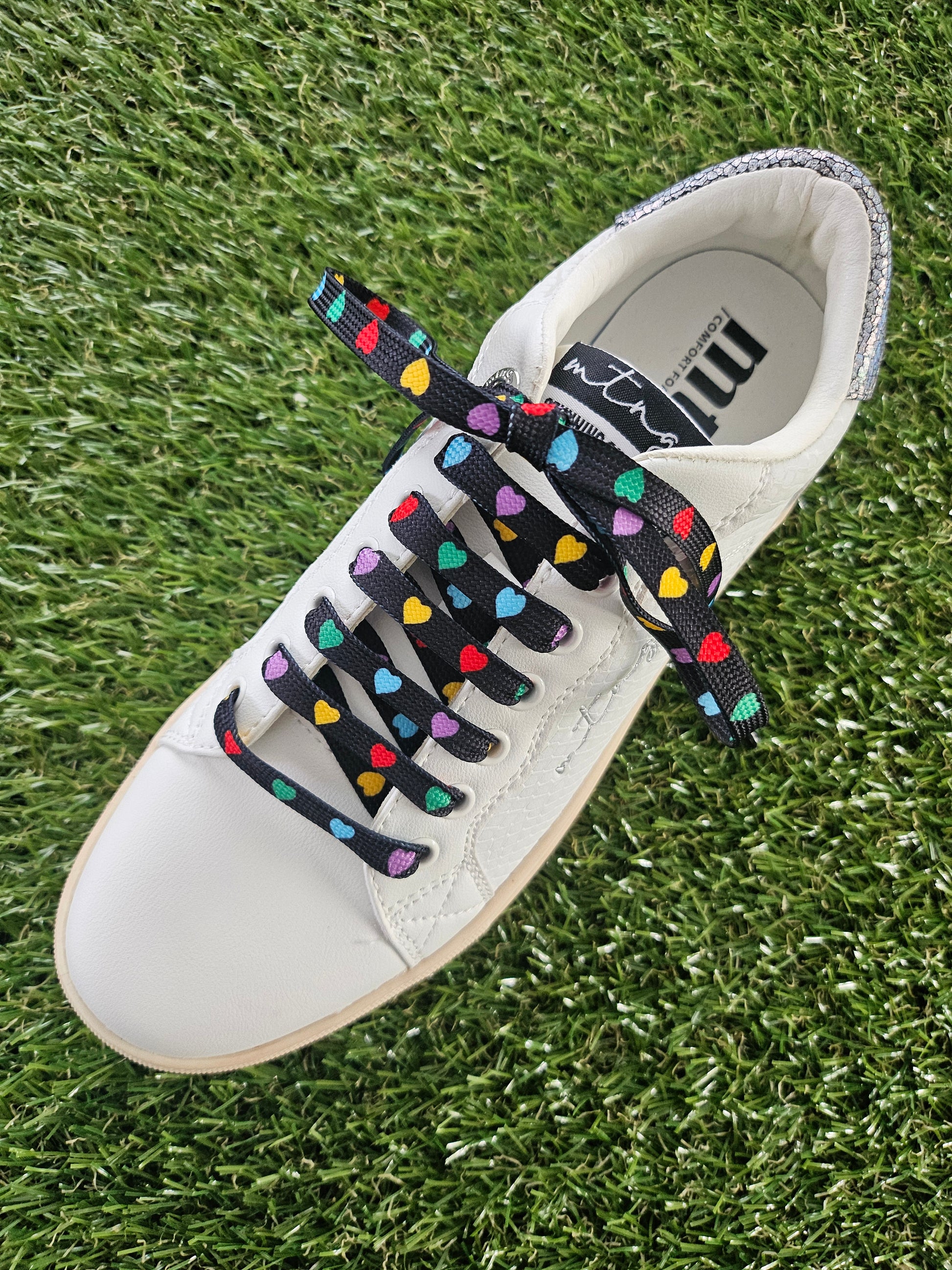 White trainer with colorful heart-patterned laces on grass