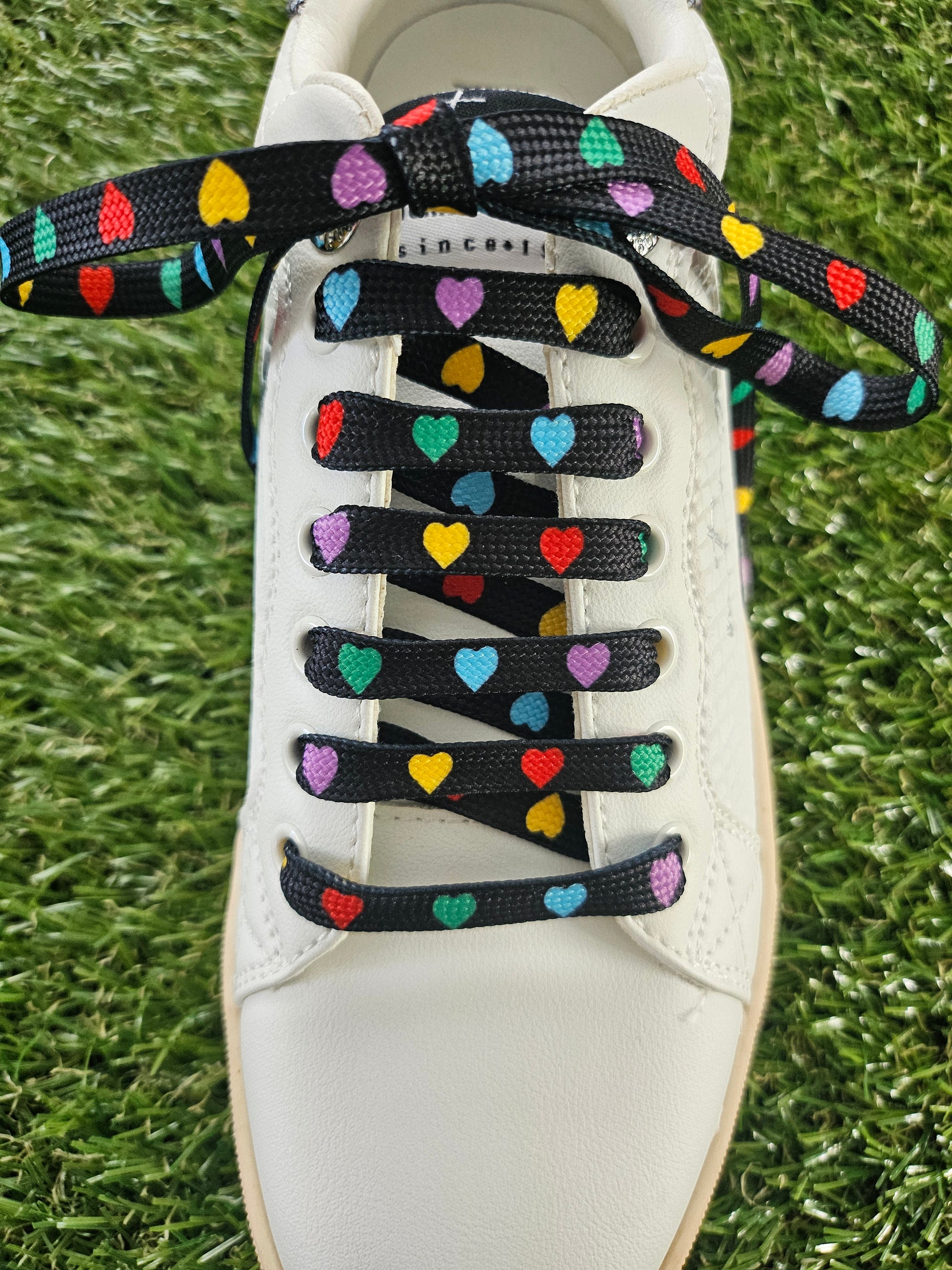 White shoe with colorful heart-patterned shoelaces on a grass background