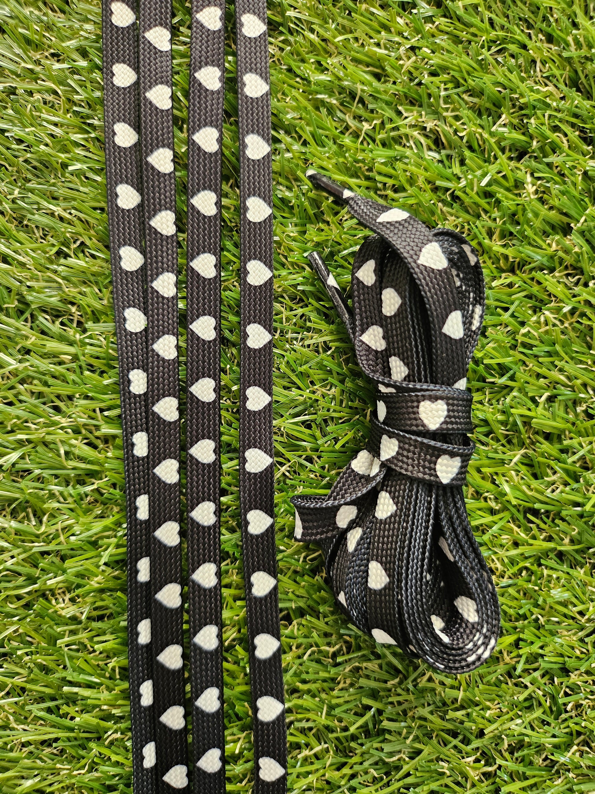 Black shoelace with white heart patterns on a grass background