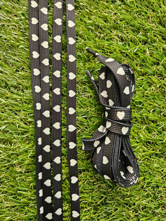 Black shoelace with white heart patterns on a grass background