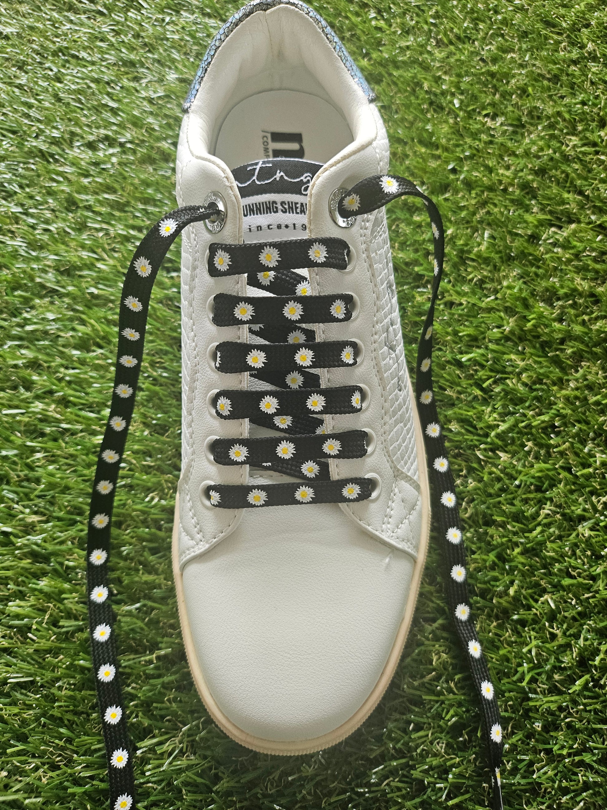 White trainer with black and white daisy flower laces on grass