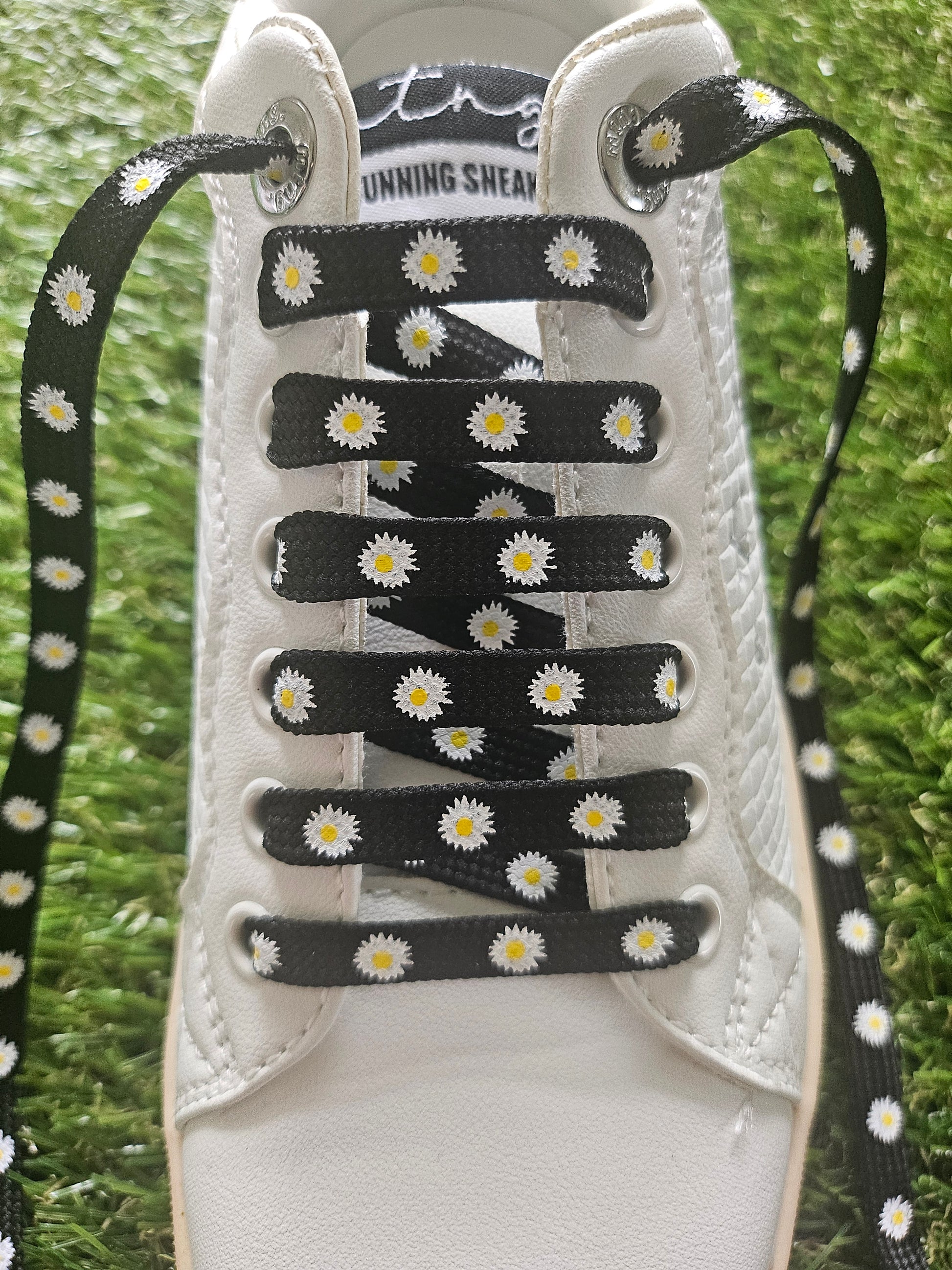 White sneaker with black and white daisy-patterned shoelaces on a grass background