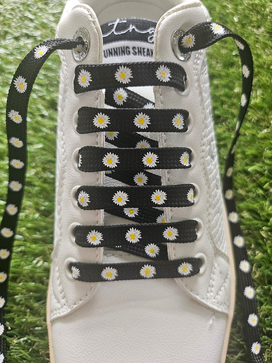 White sneaker with black and white daisy-patterned shoelaces on a grass background