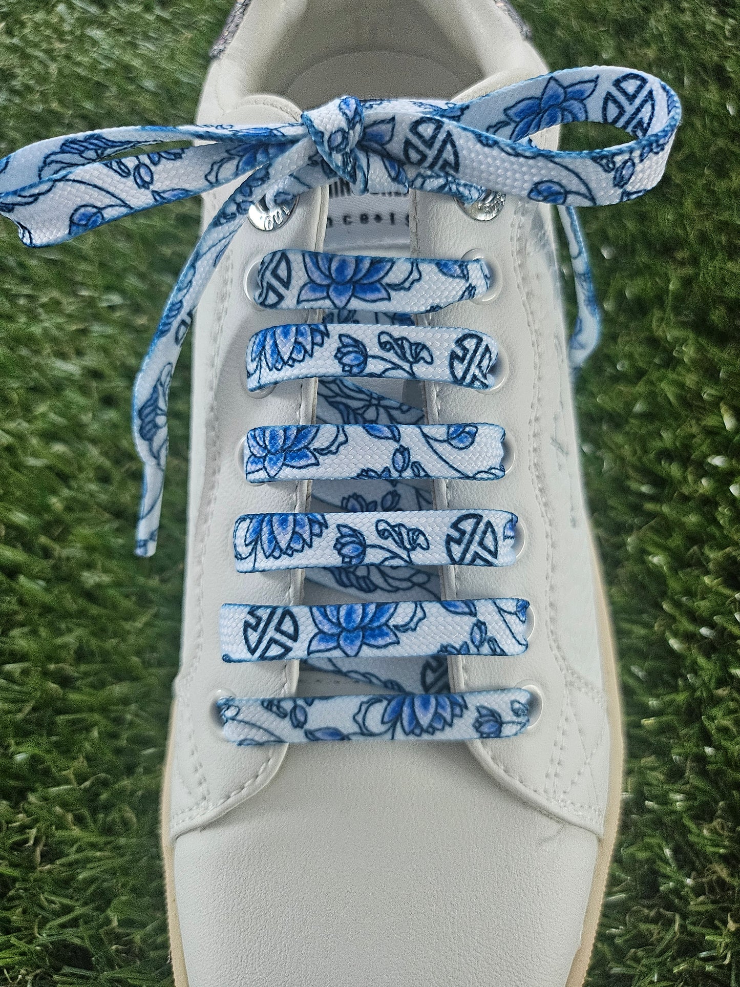 White sneaker with blue floral-patterned shoelaces on a grass background