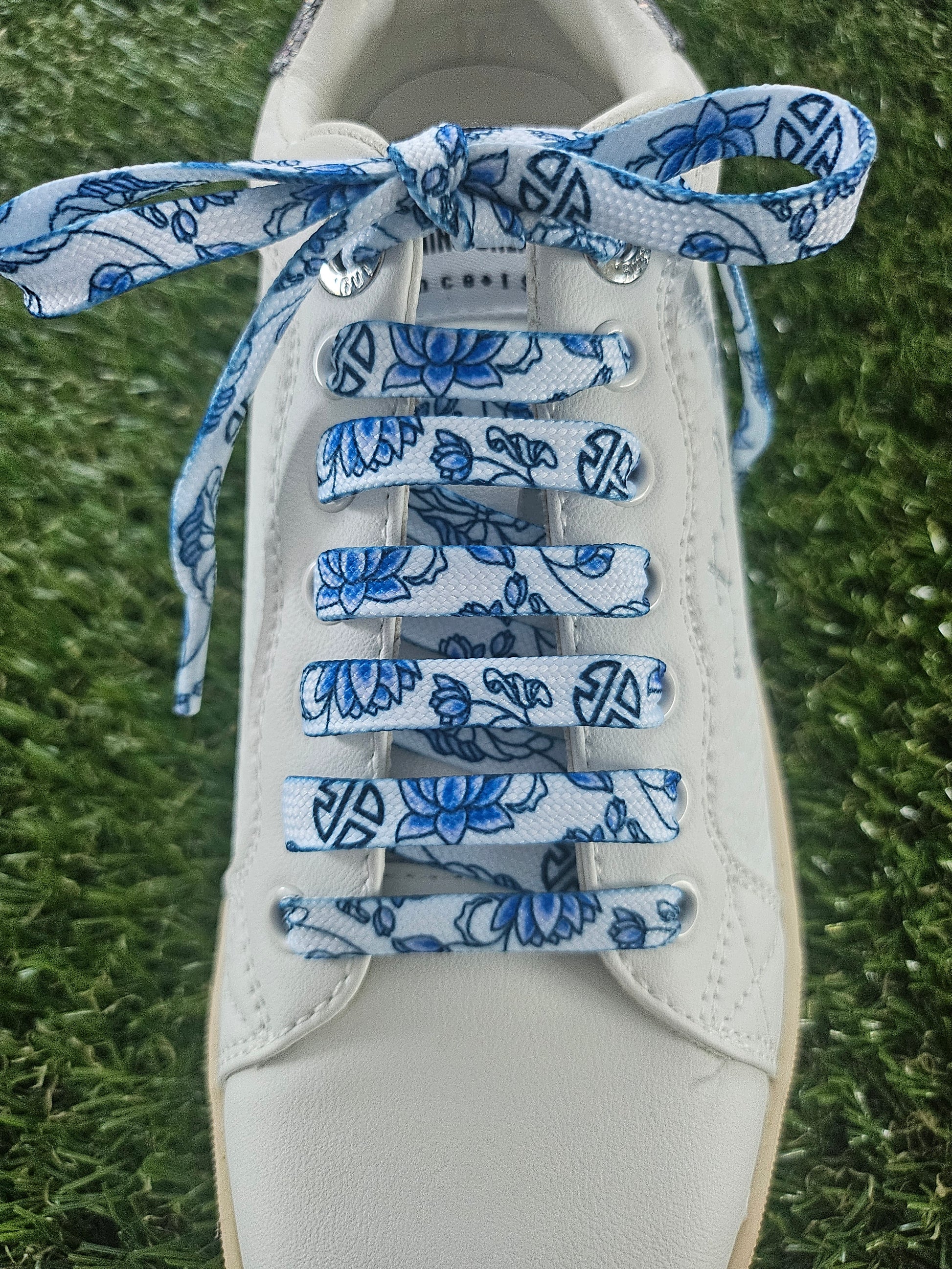 White sneaker with blue floral-patterned shoelaces on a grass background