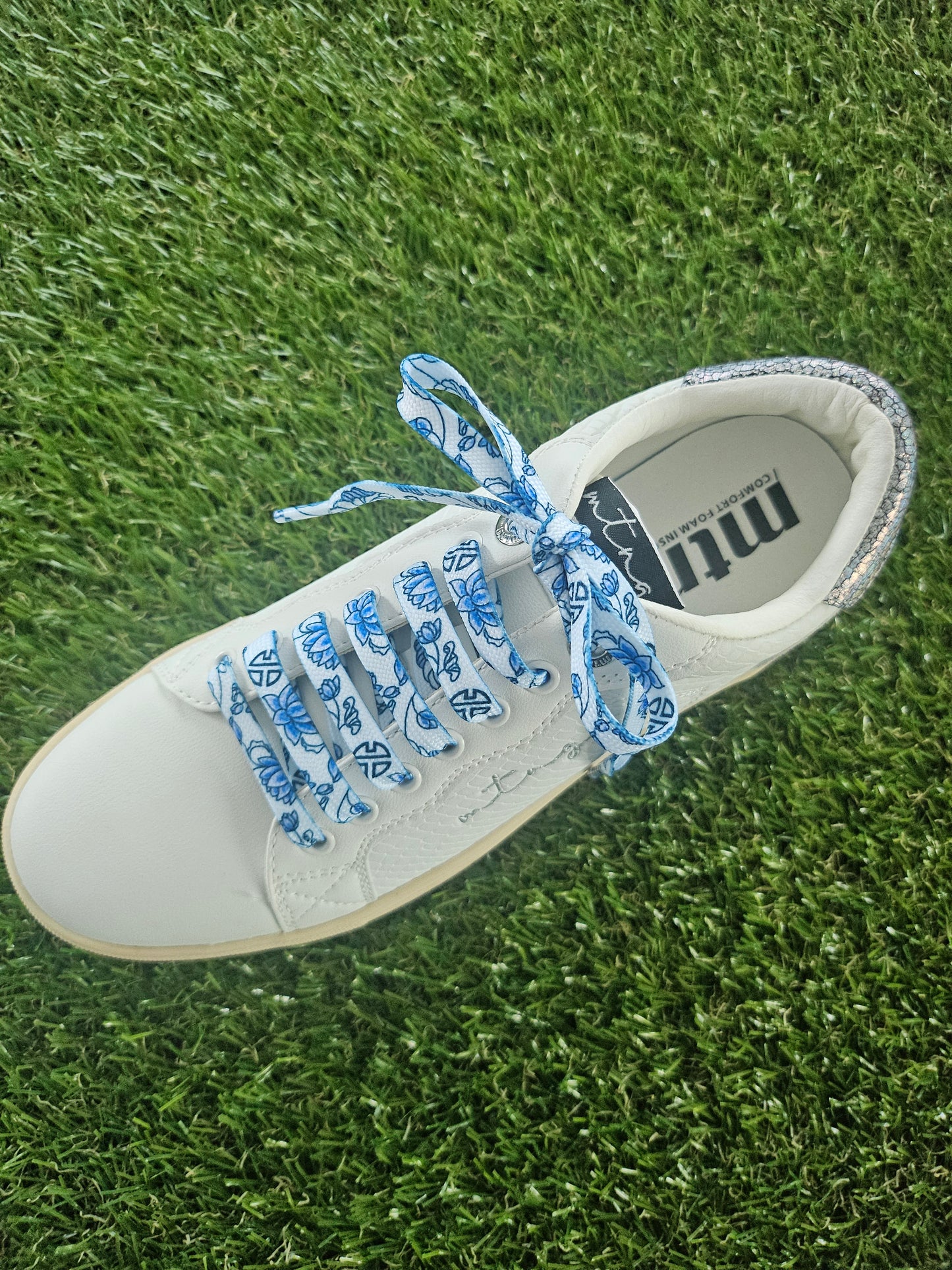 White sneaker with blue laces on grass