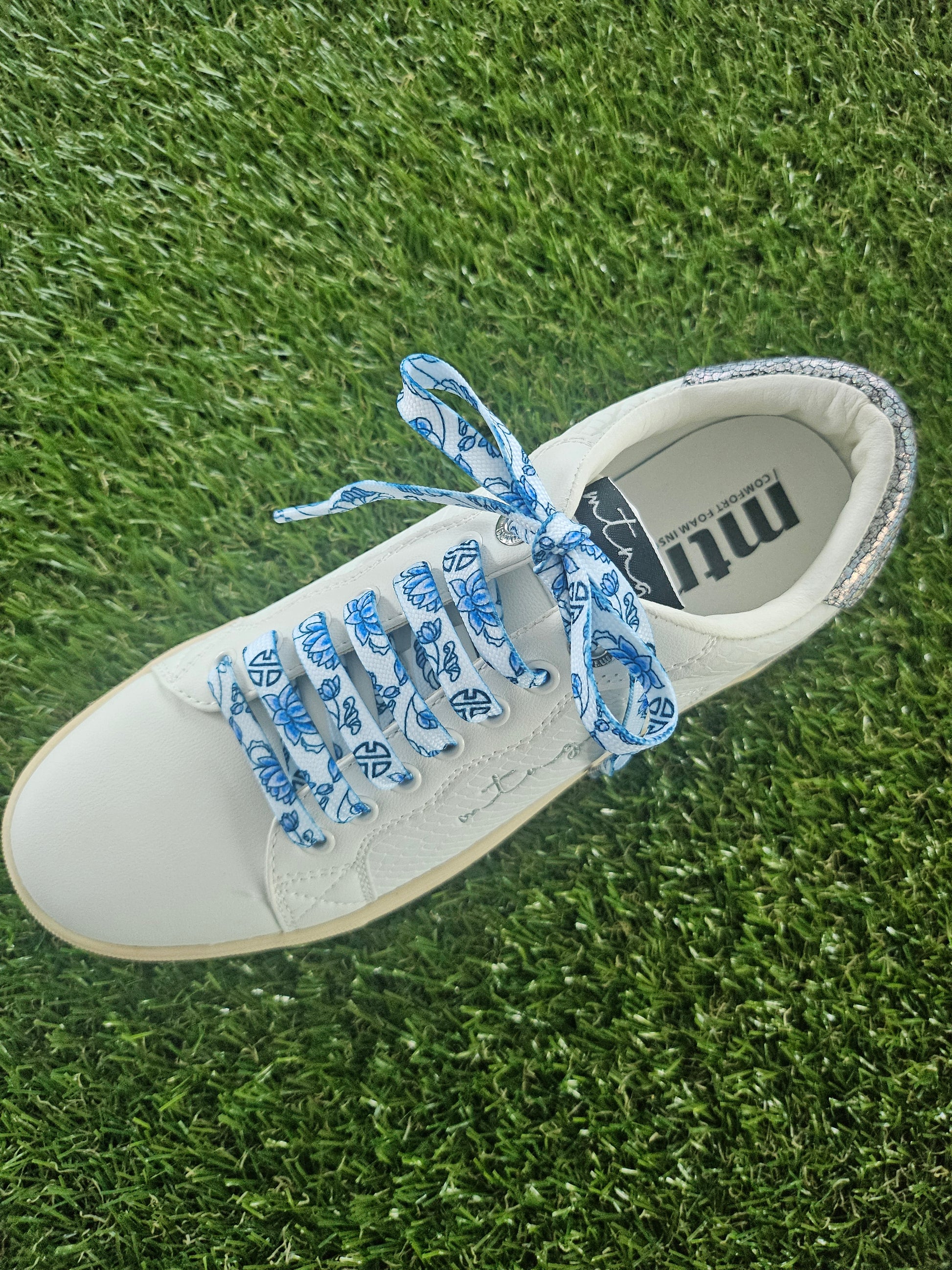 White sneaker with blue laces on grass