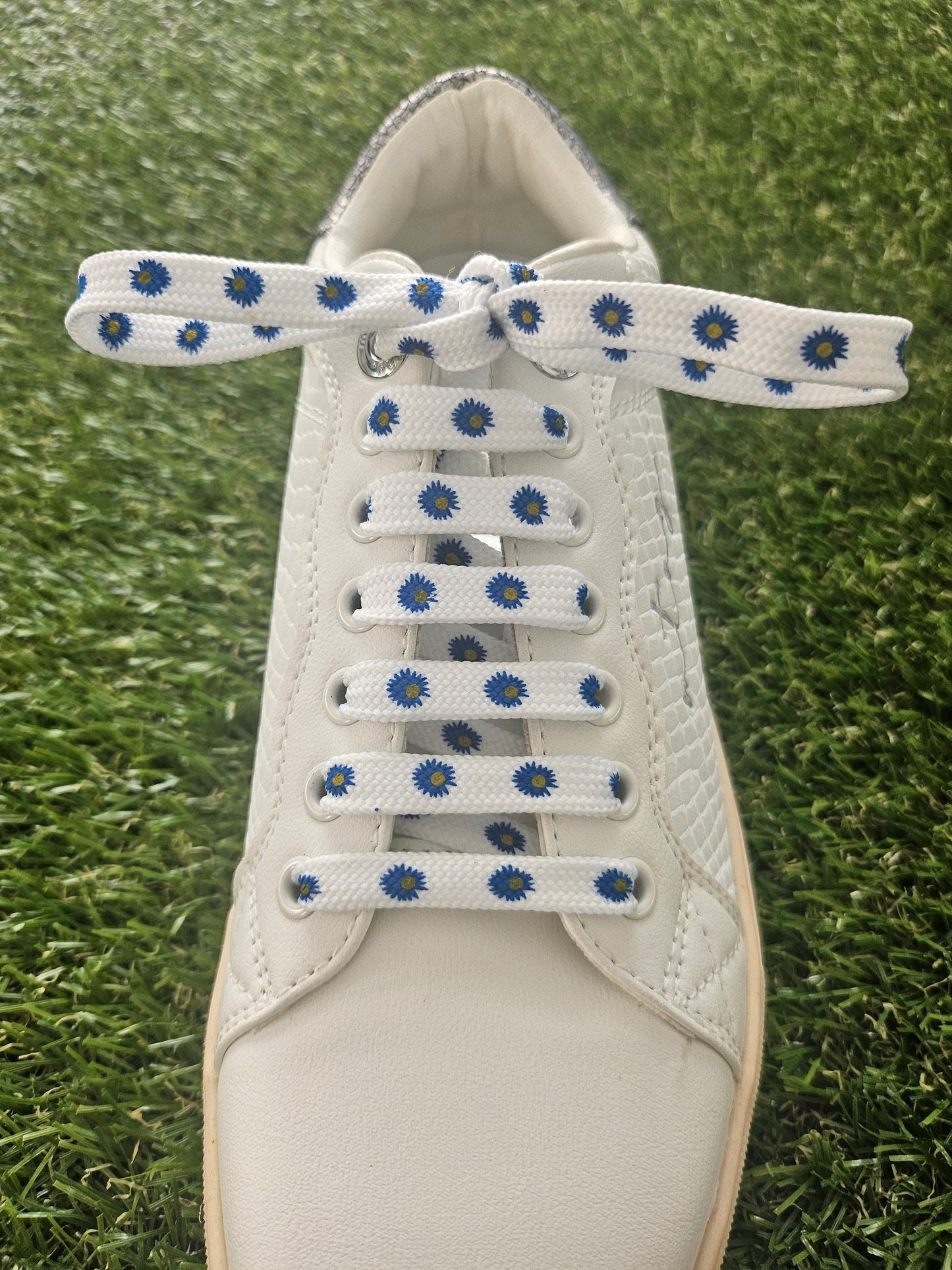White sneaker with blue and white dairy flowers shoelaces on a grass background