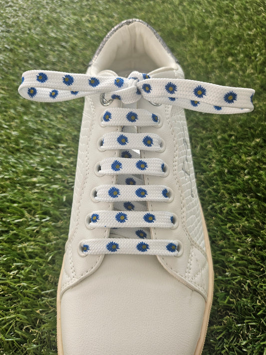 White sneaker with blue and white dairy flowers shoelaces on a grass background