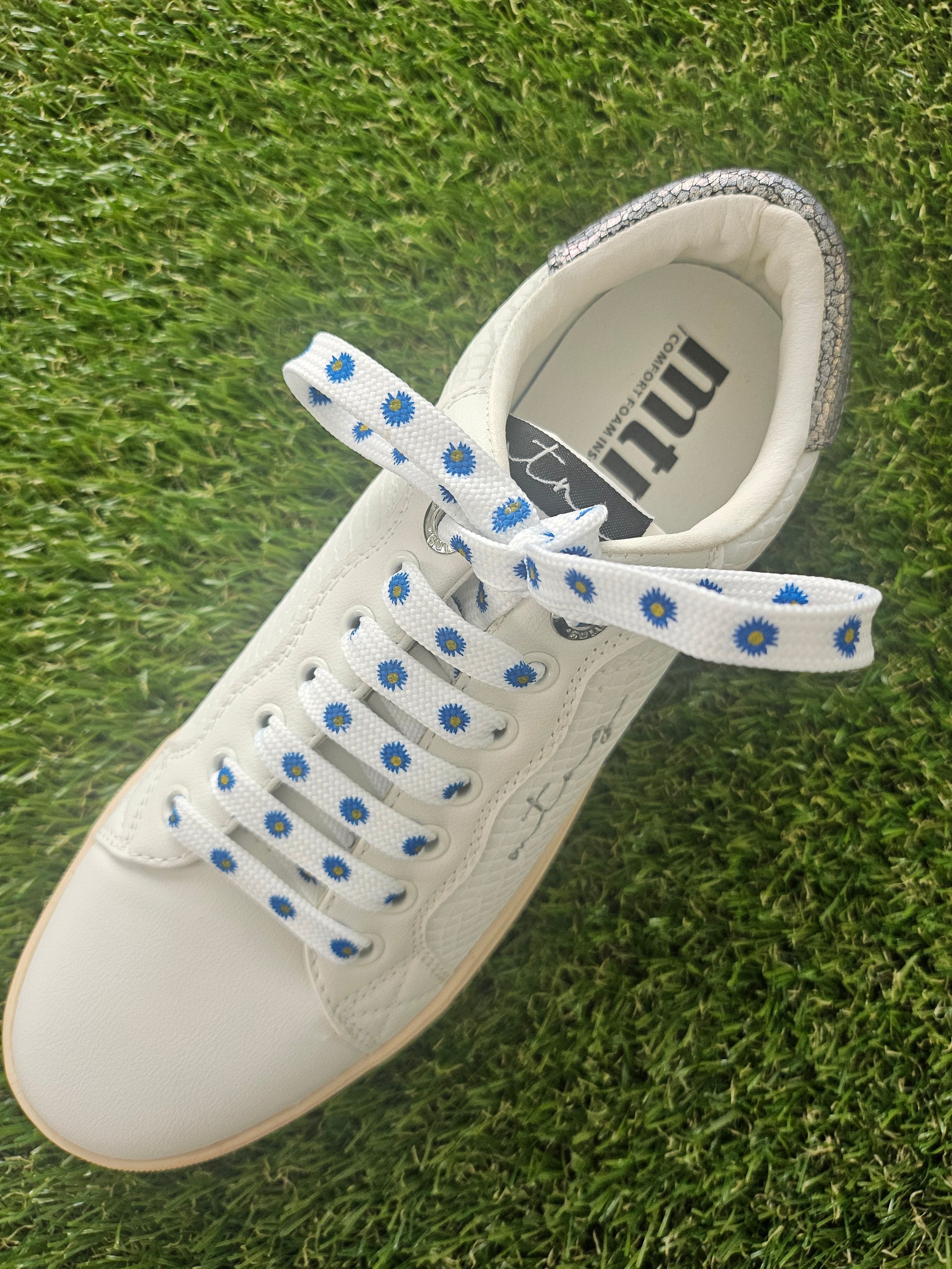 White sneaker with blue and white dairy flowers shoelaces on green grass