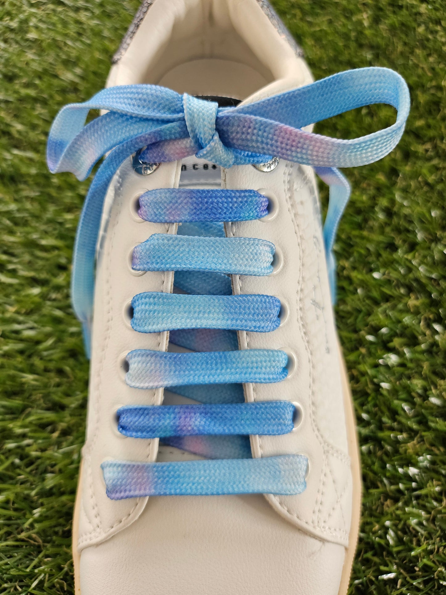 Close-up of a shoe with blue gradient shoelaces on grass.