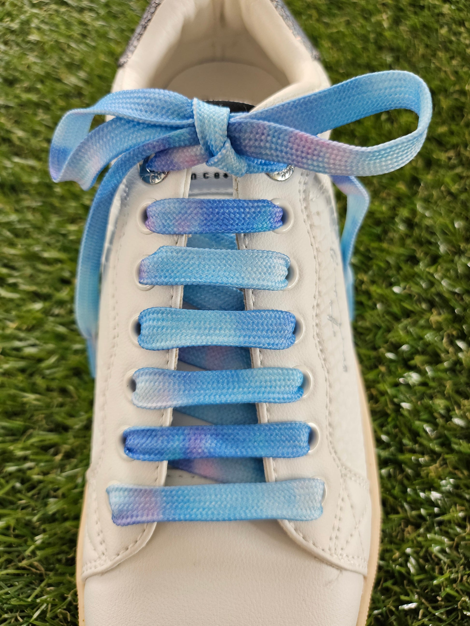 Close-up of a shoe with blue gradient shoelaces on grass.