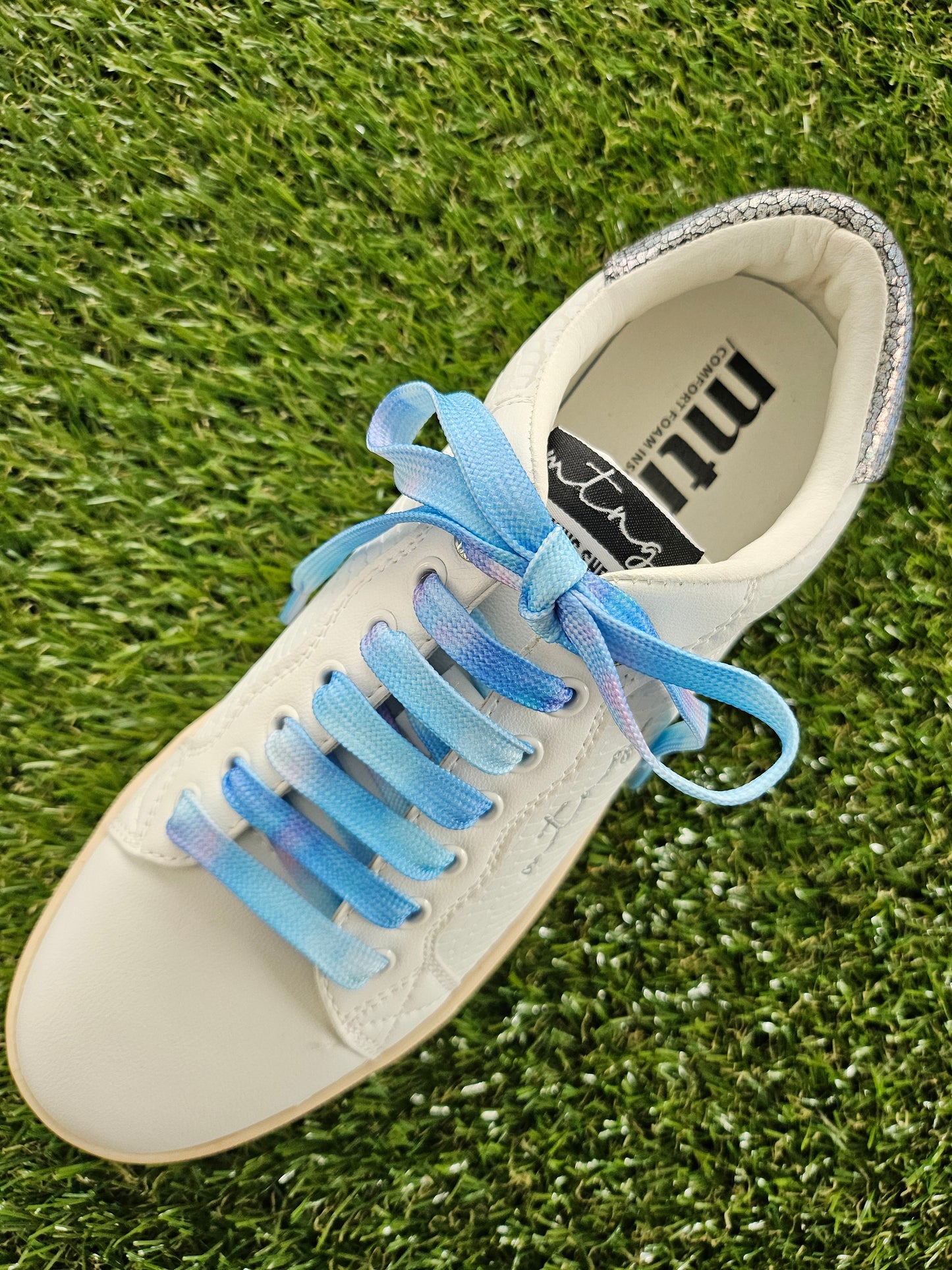 White sneaker with blue laces on grass, featuring the brand 'mtv'.