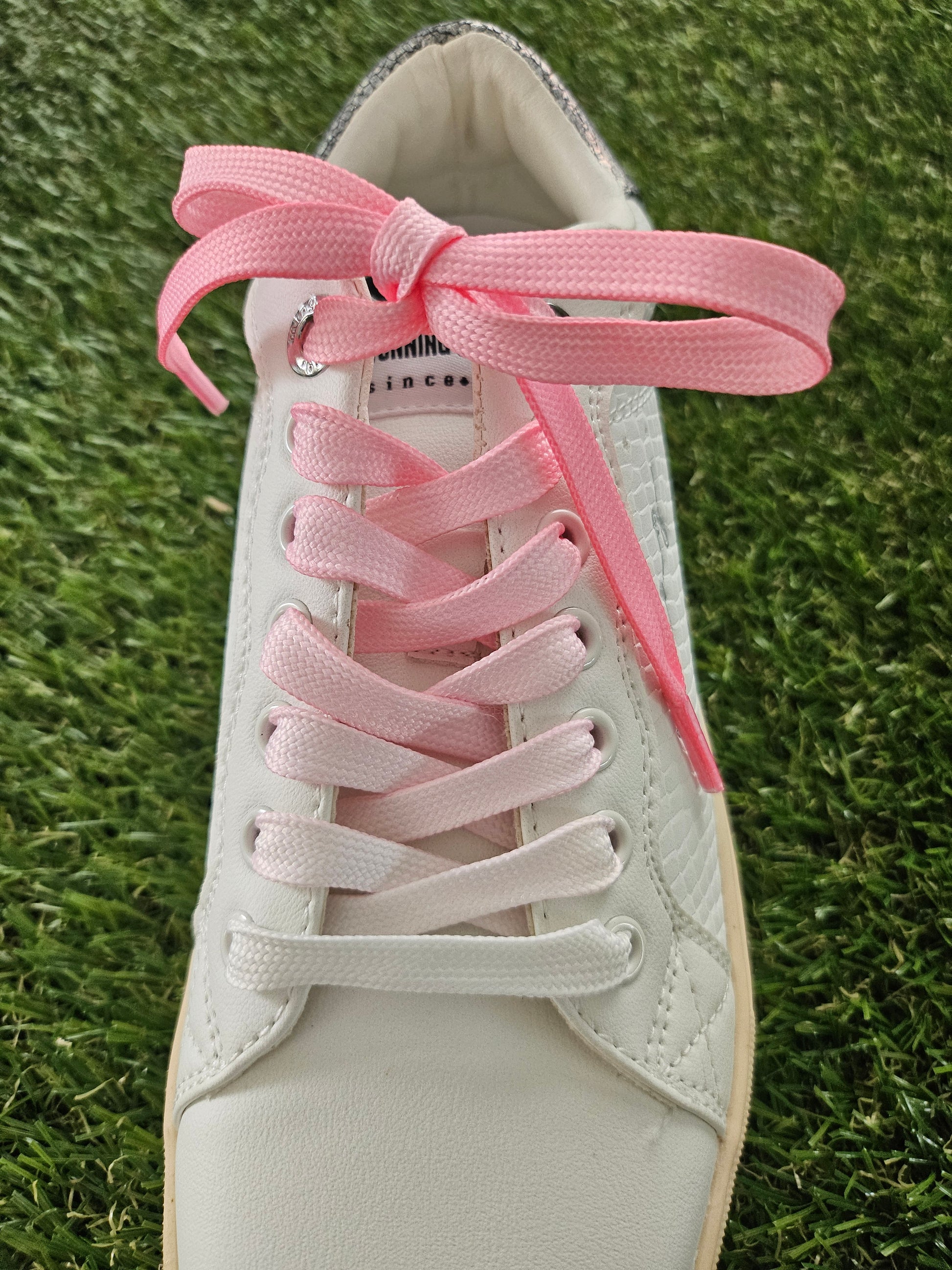 White sneaker with pink shoelaces on a grass background