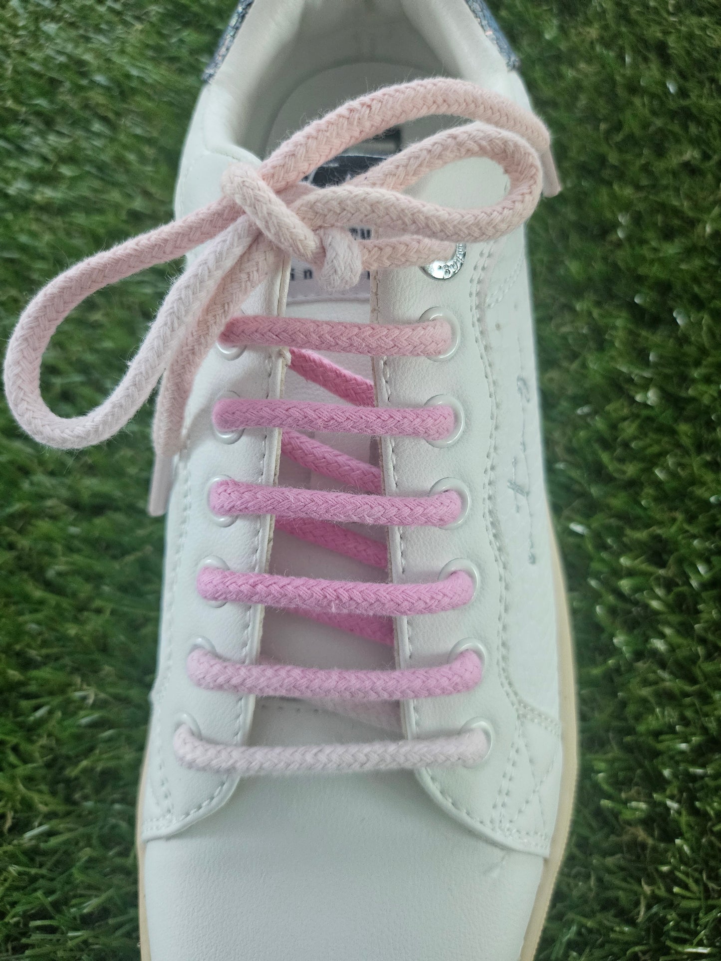 White sneaker with pink shoelaces on a grass background