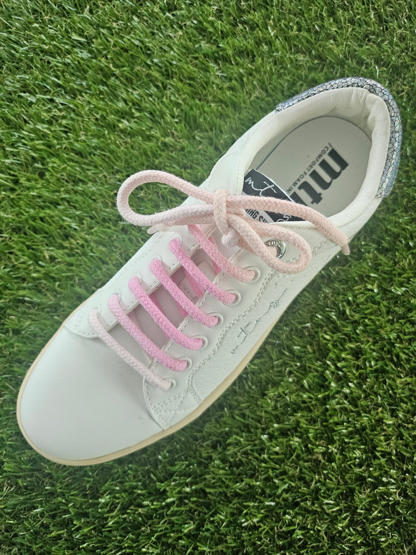 White sneaker with pink laces on grass